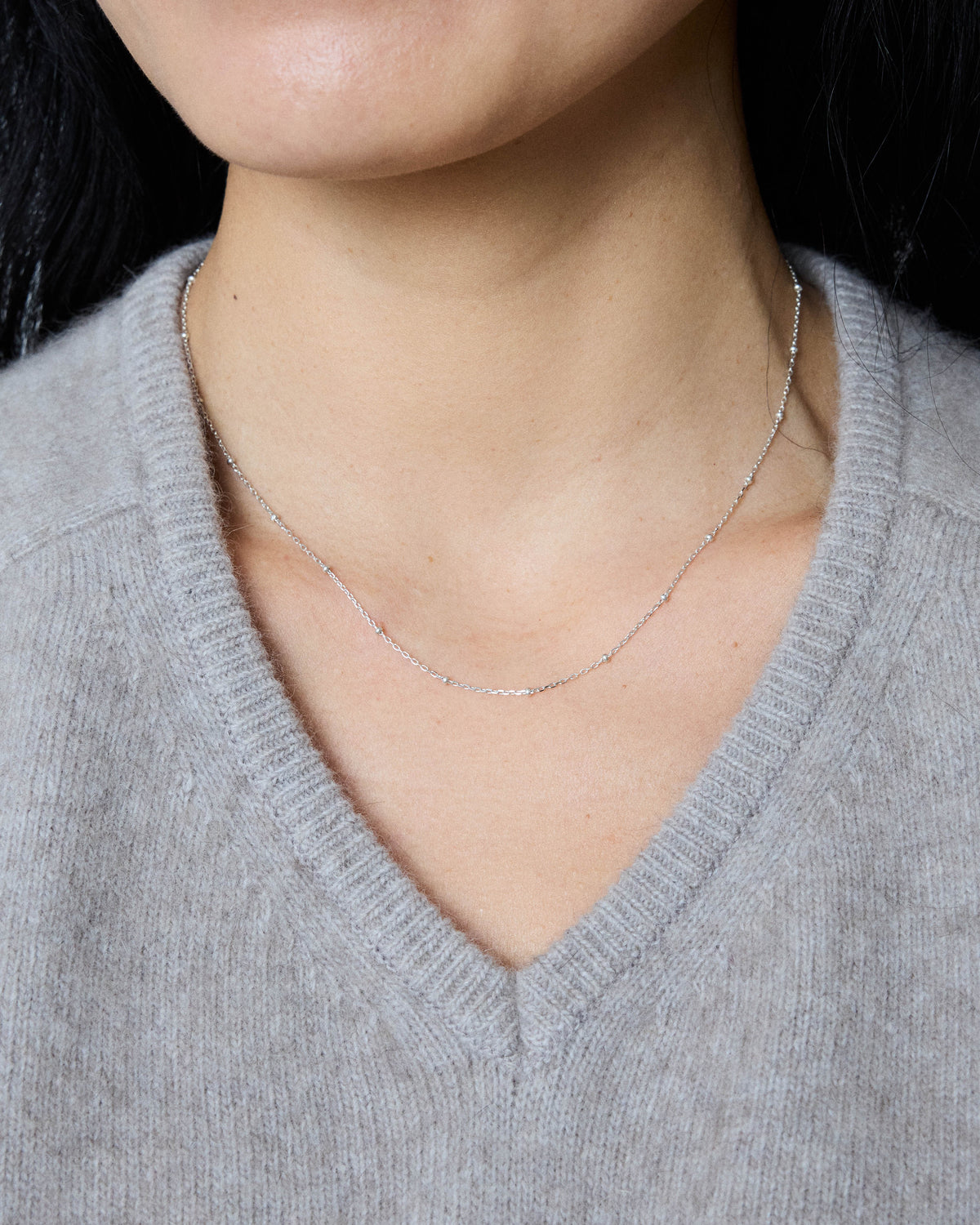 Silver ball station necklace layered at the collarbone with a gray sweater – HANNA543 N1057 starlit dot chain