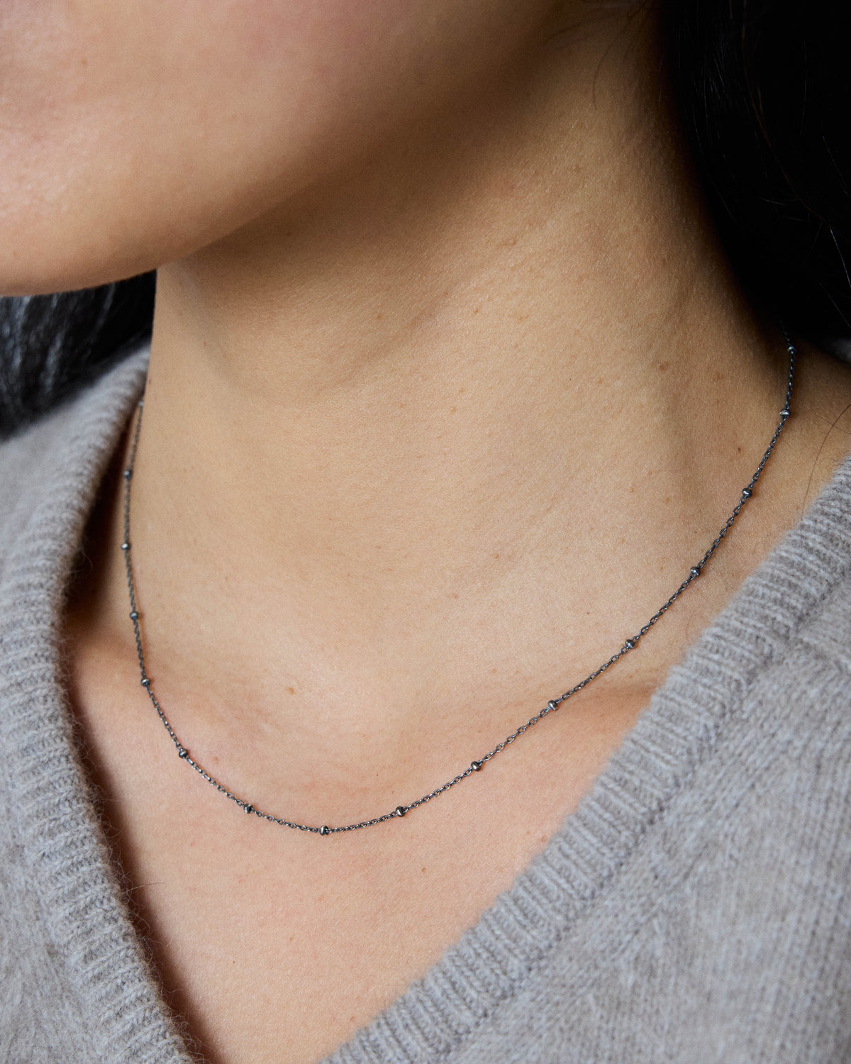 Model wearing an antique silver ball station chain necklace with a gray V-neck sweater – HANNA543 N1057 starlit dot chain