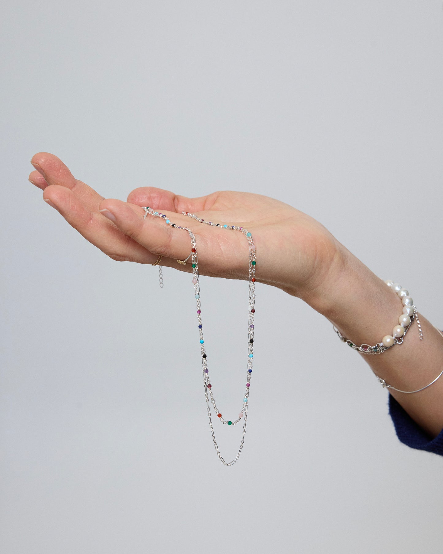 Layered sterling silver necklace with colorful gemstone accents draped over hand