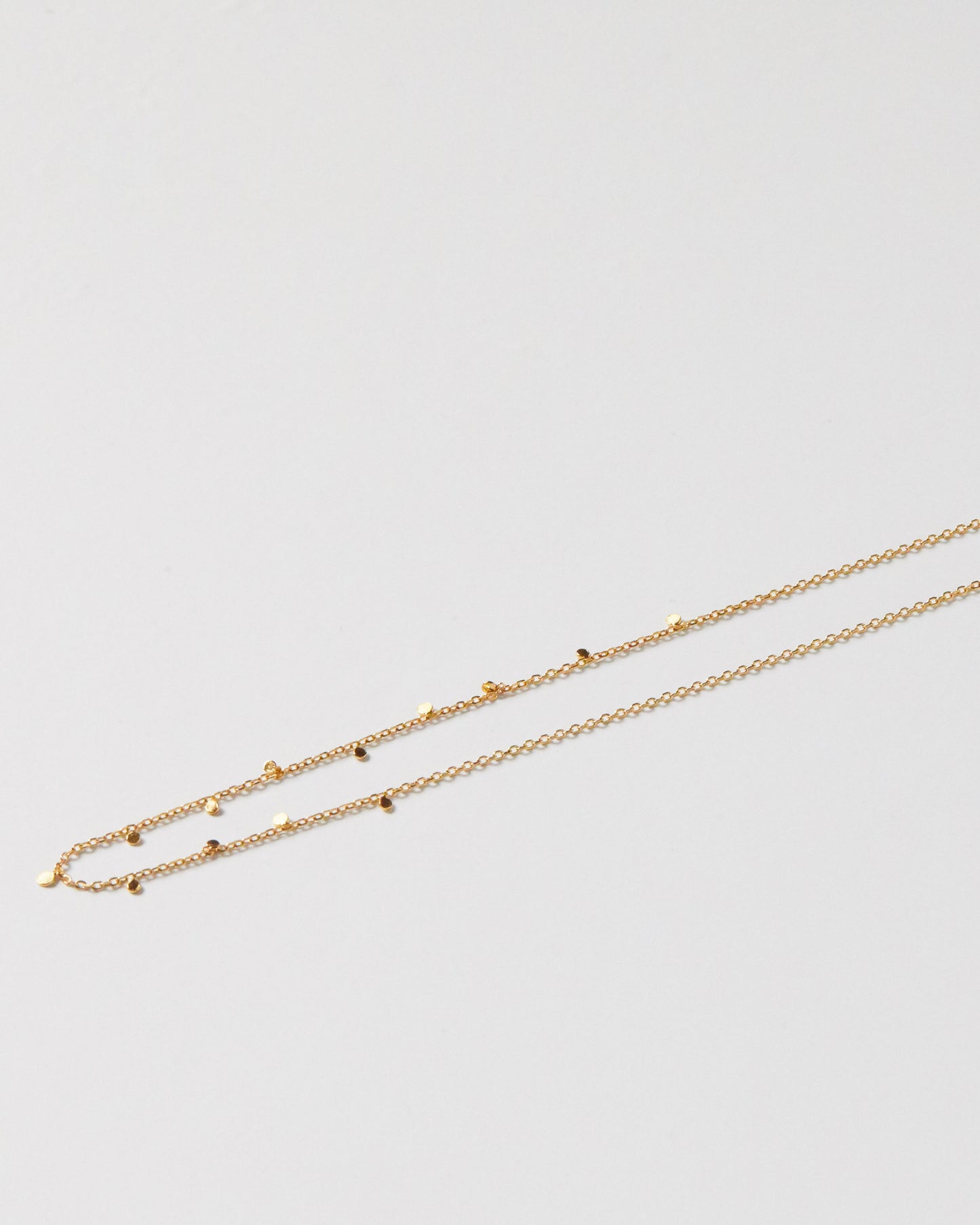Close-up of gold necklace with tiny disc details on collarbone