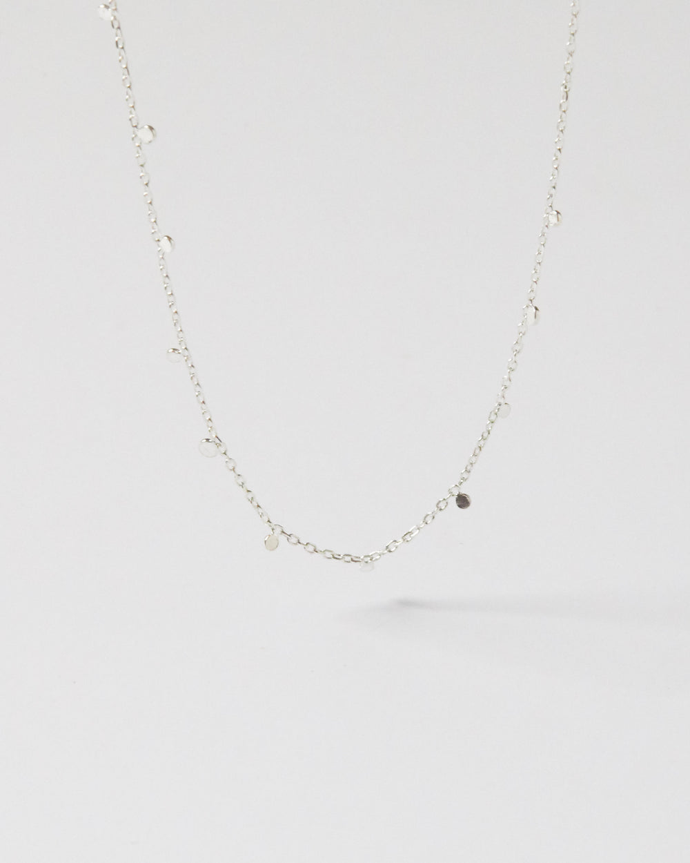 Hanging silver necklace with small discs against clean white background