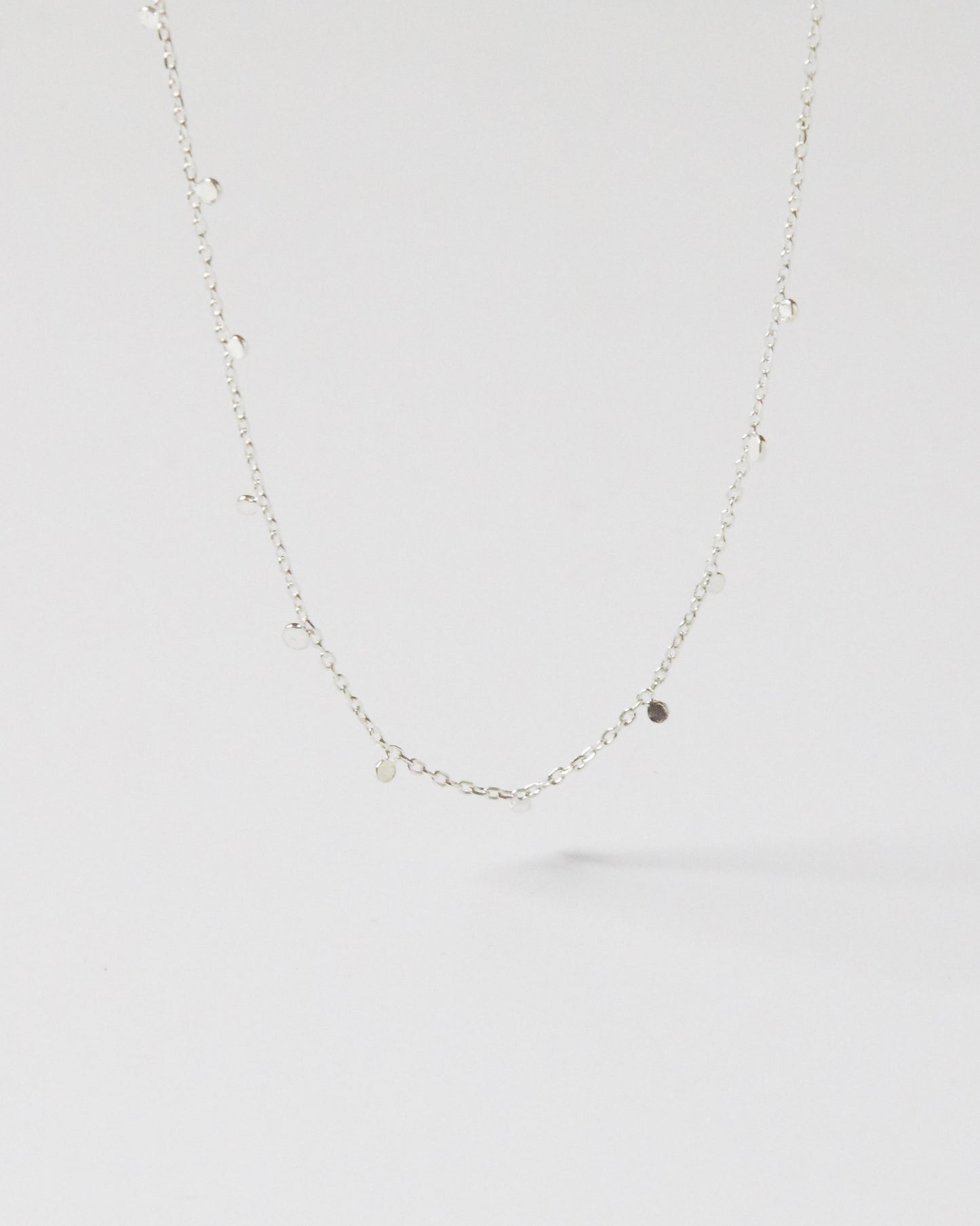 Hanging silver necklace with small discs against clean white background