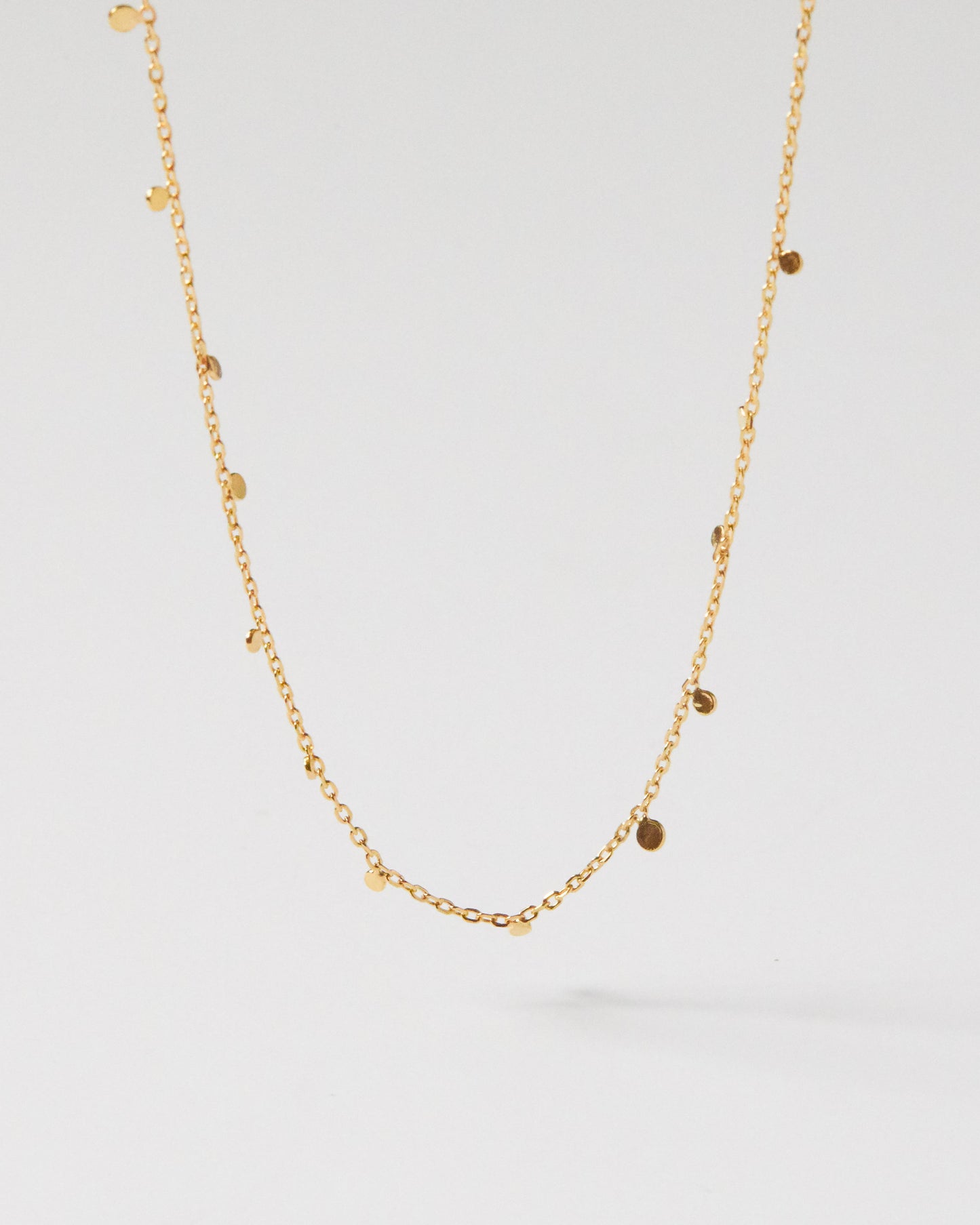 Hanging gold necklace with small discs against clean white background