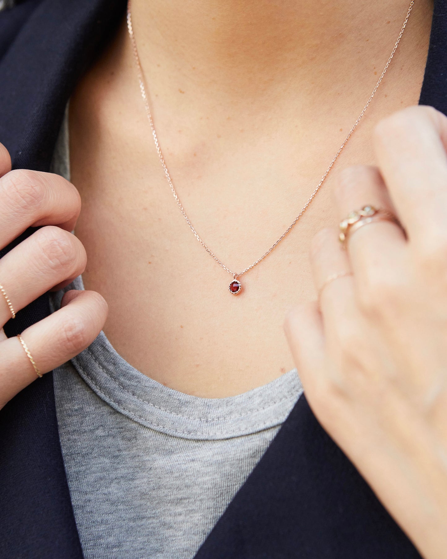 Person wearing a delicate necklace with a small red gemstone, close-up of the necklace and part of the person's chest.