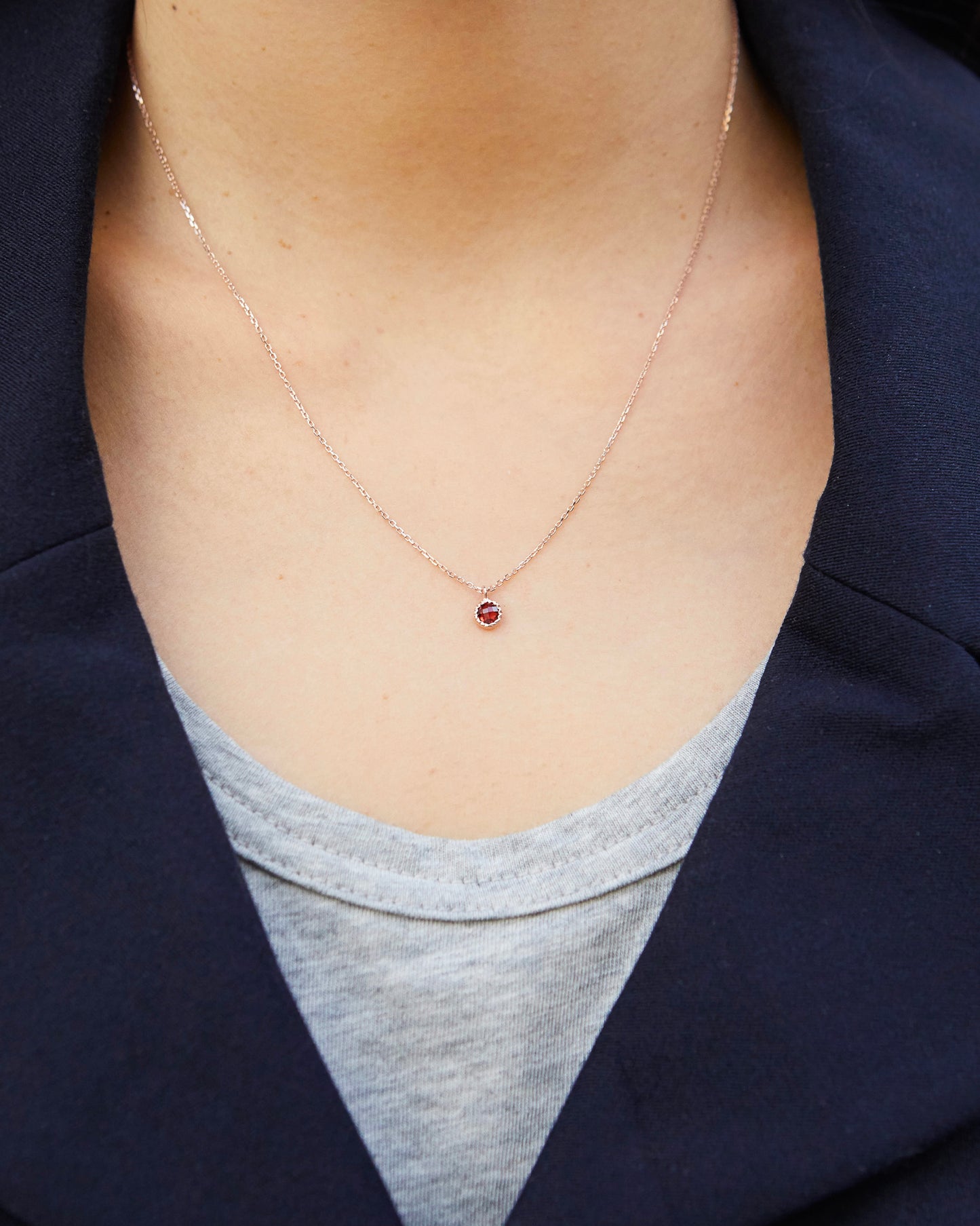 Necklace with a red pendant worn by a person, with a dark jacket and gray shirt in the background.