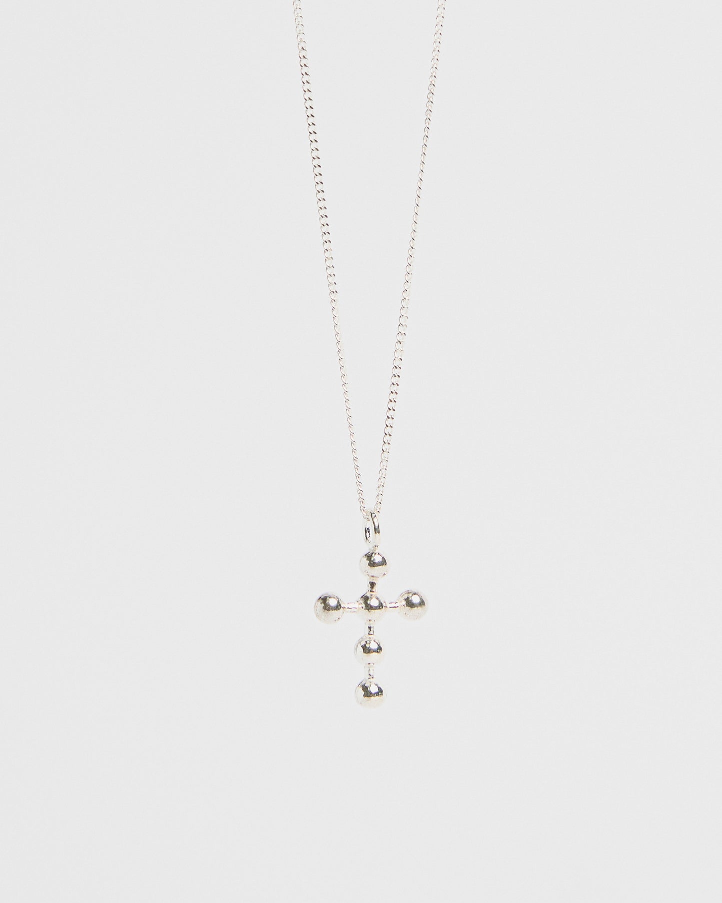 Silver cross pendant with orb accents, hanging from fine chain, isolated on white