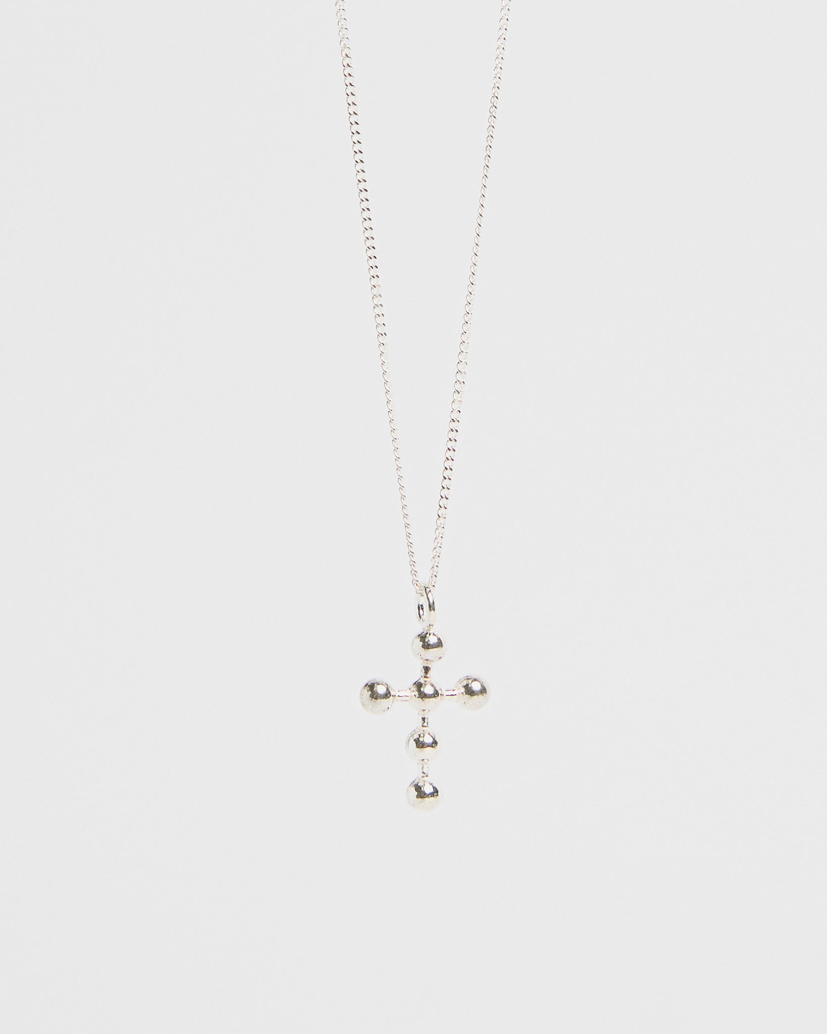 Silver cross pendant with orb accents, hanging from fine chain, isolated on white