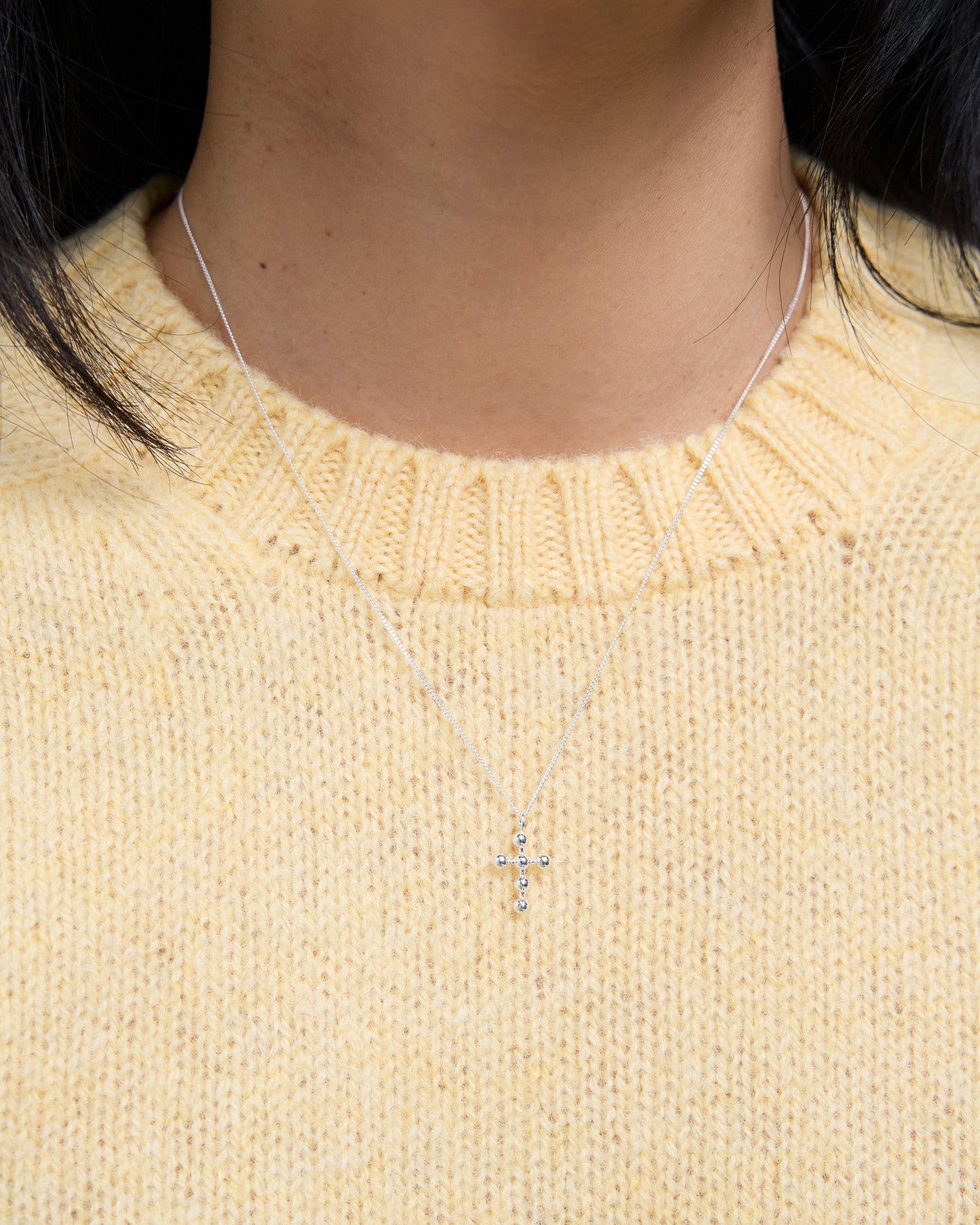 Close-up of silver cross necklace with beaded accents, worn over soft yellow knit