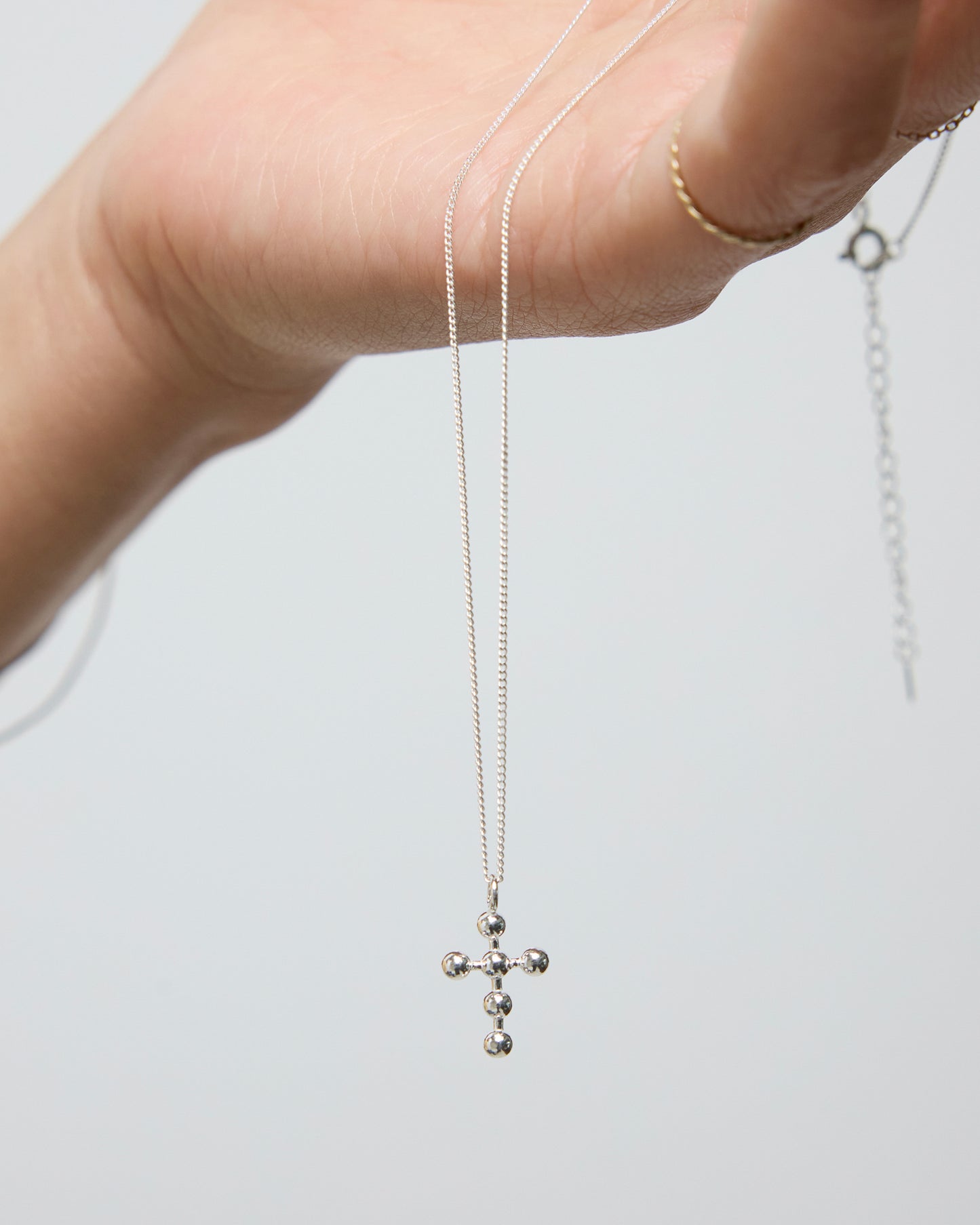 Delicate silver cross necklace held in palm, showing beaded pendant detail