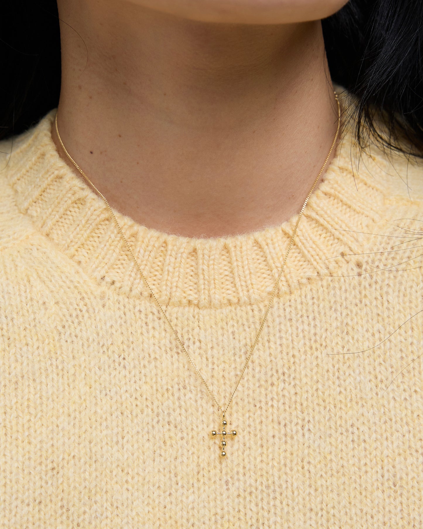 Gold cross necklace worn with cozy yellow knit, subtle and centered