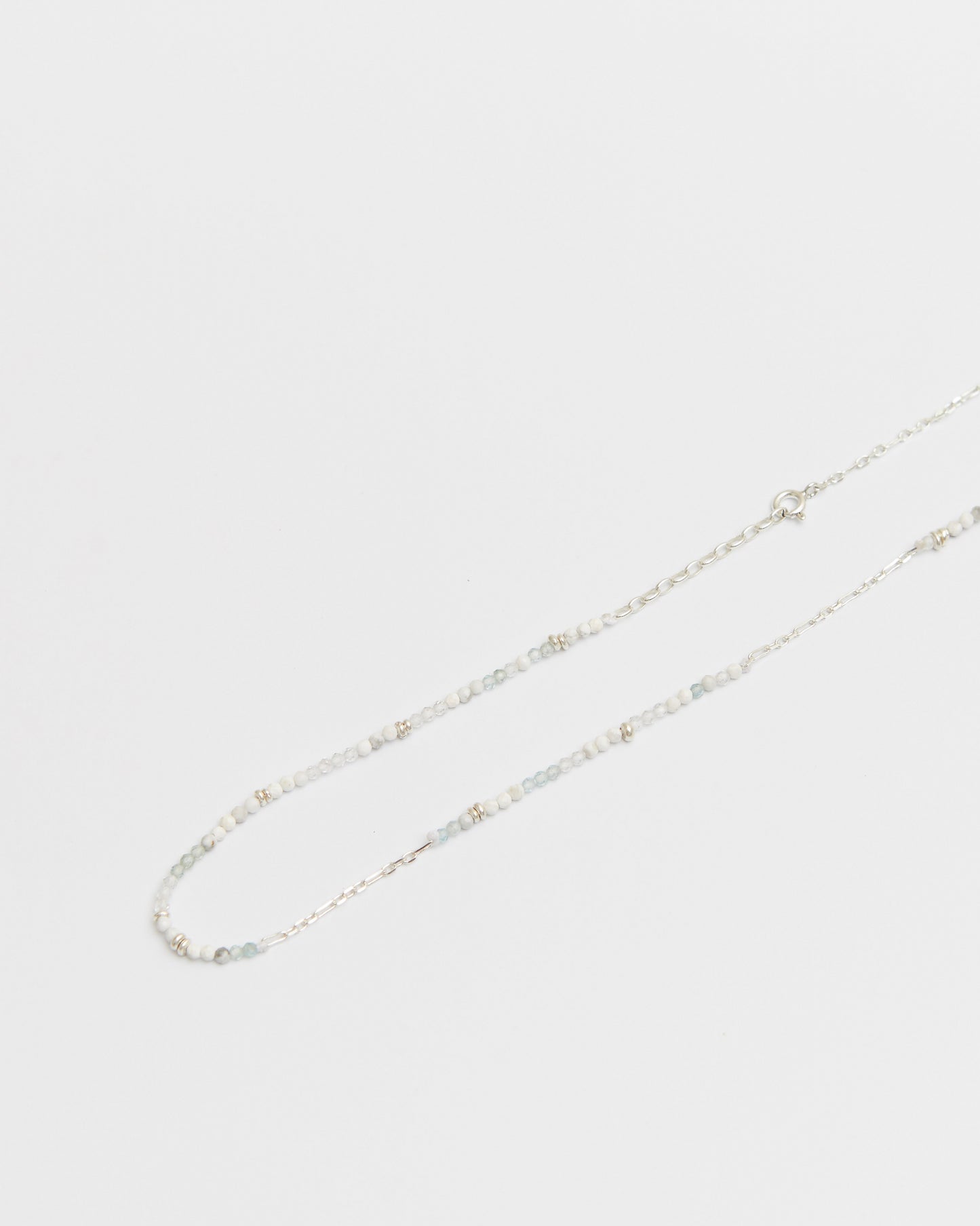 close-up of a soft-toned beaded and silver chain necklace laid flat on white background