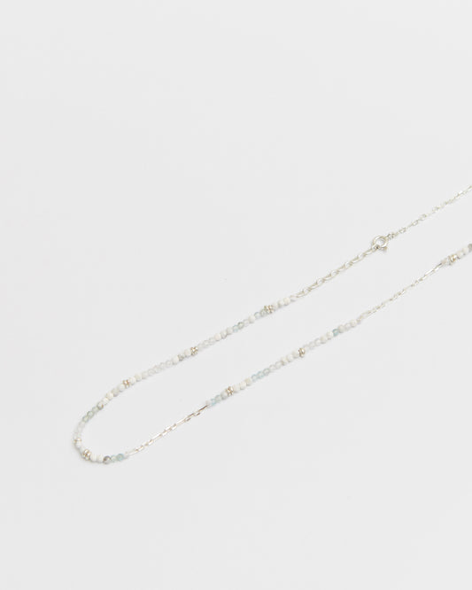 close-up of a soft-toned beaded and silver chain necklace laid flat on white background