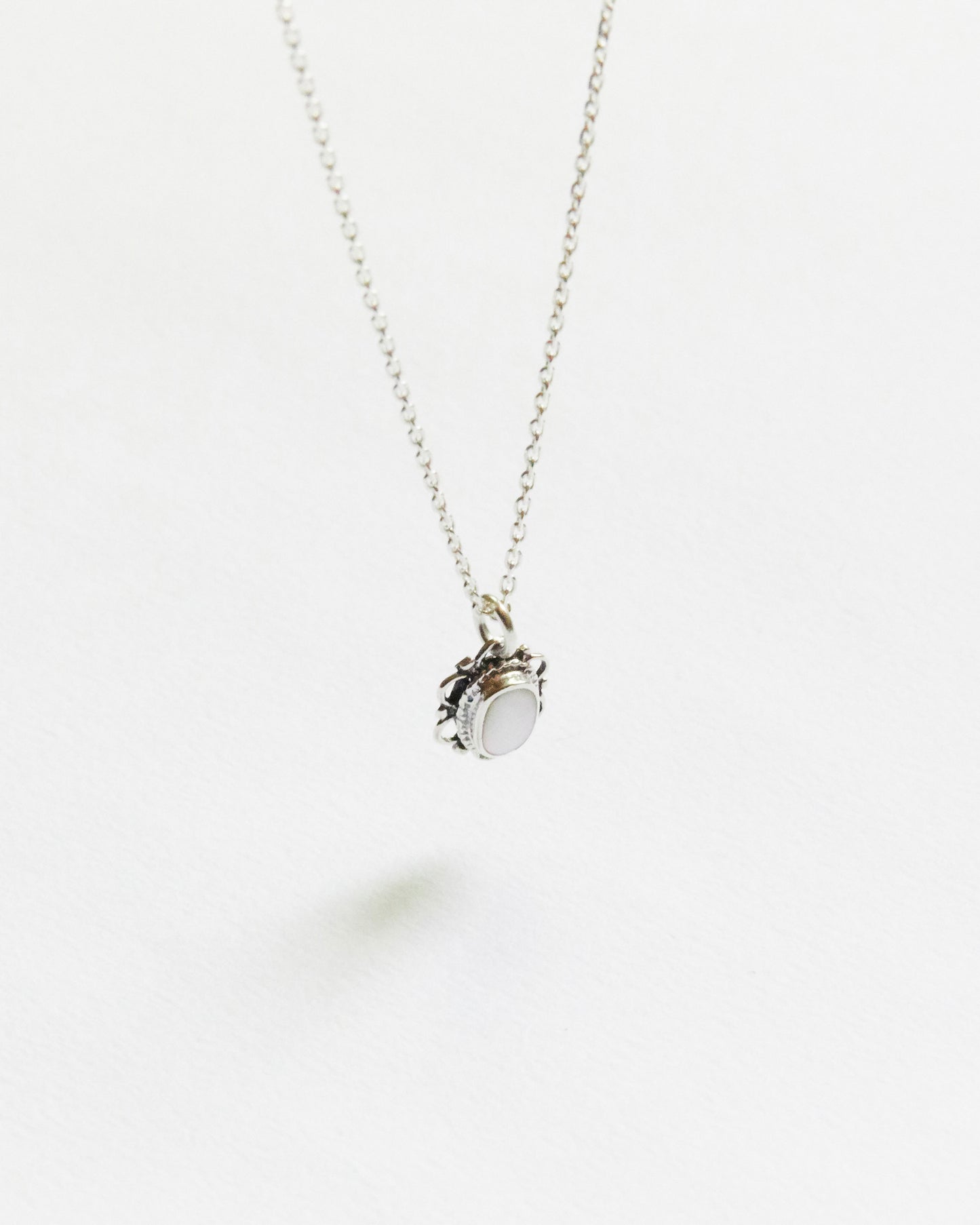 white oval stone necklace with detailed silver frame, photographed on white background