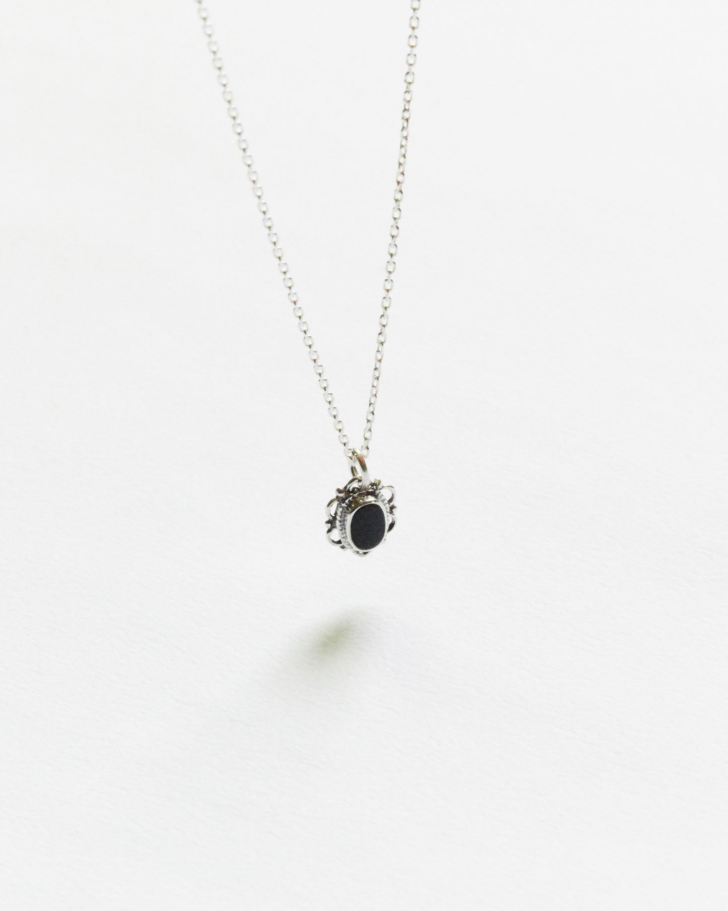 Close-up of black oval stone pendant in ornate silver frame on white background