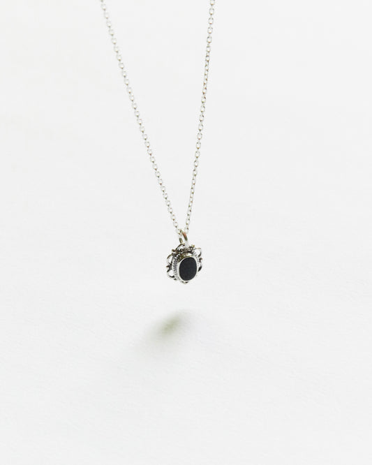 Close-up of black oval stone pendant in ornate silver frame on white background