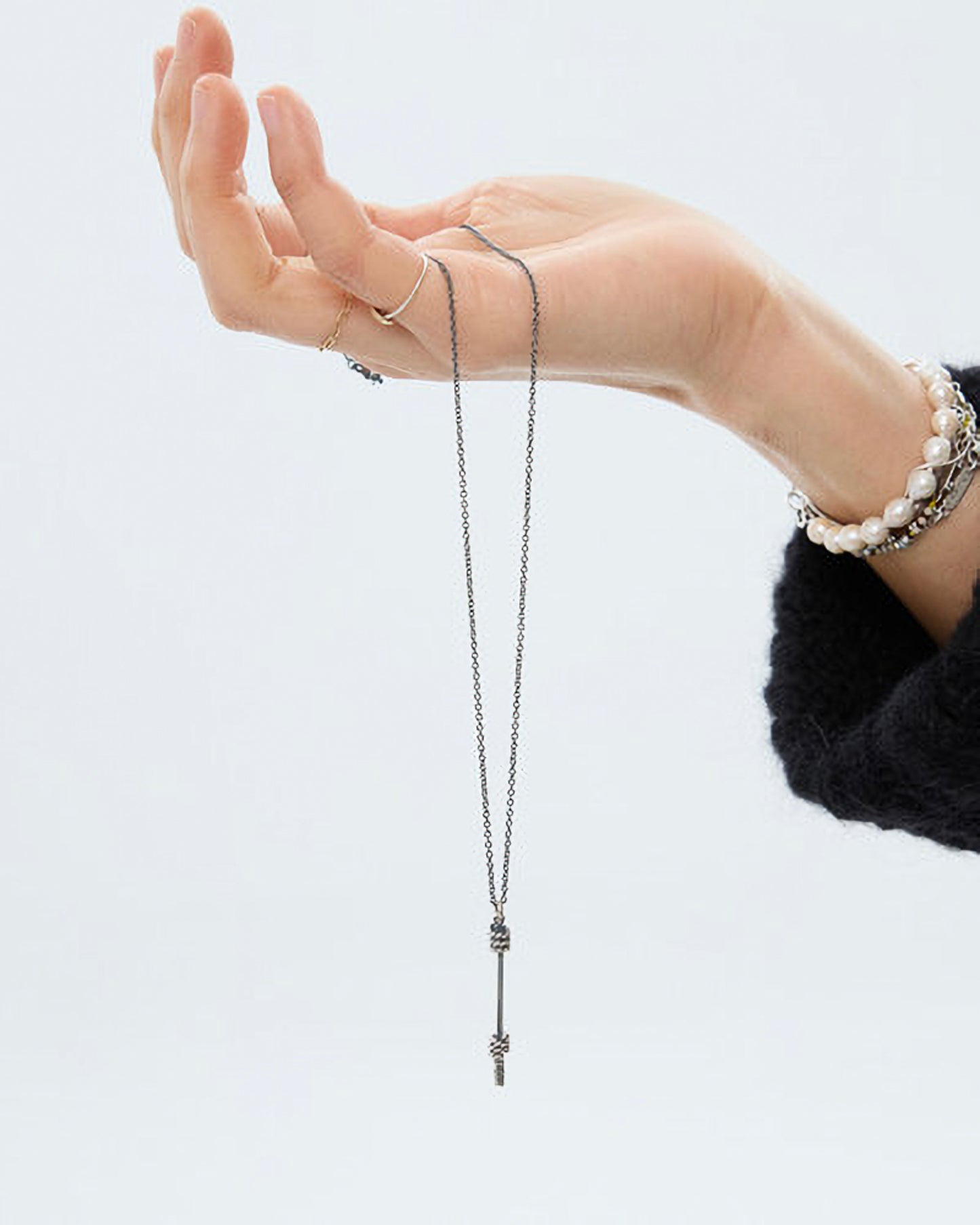 Hand wearing a delicate silver necklace against a plain background