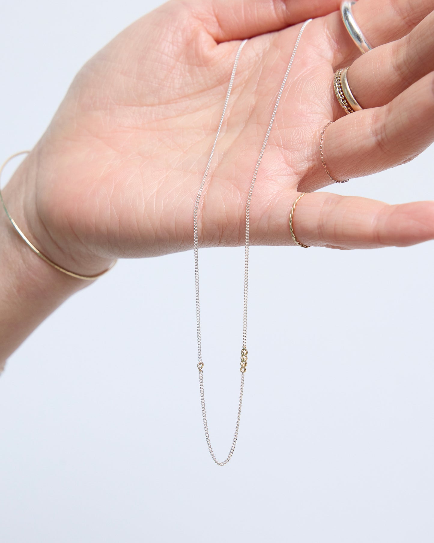 Hand holding minimalist silver chain necklace with small gold link details