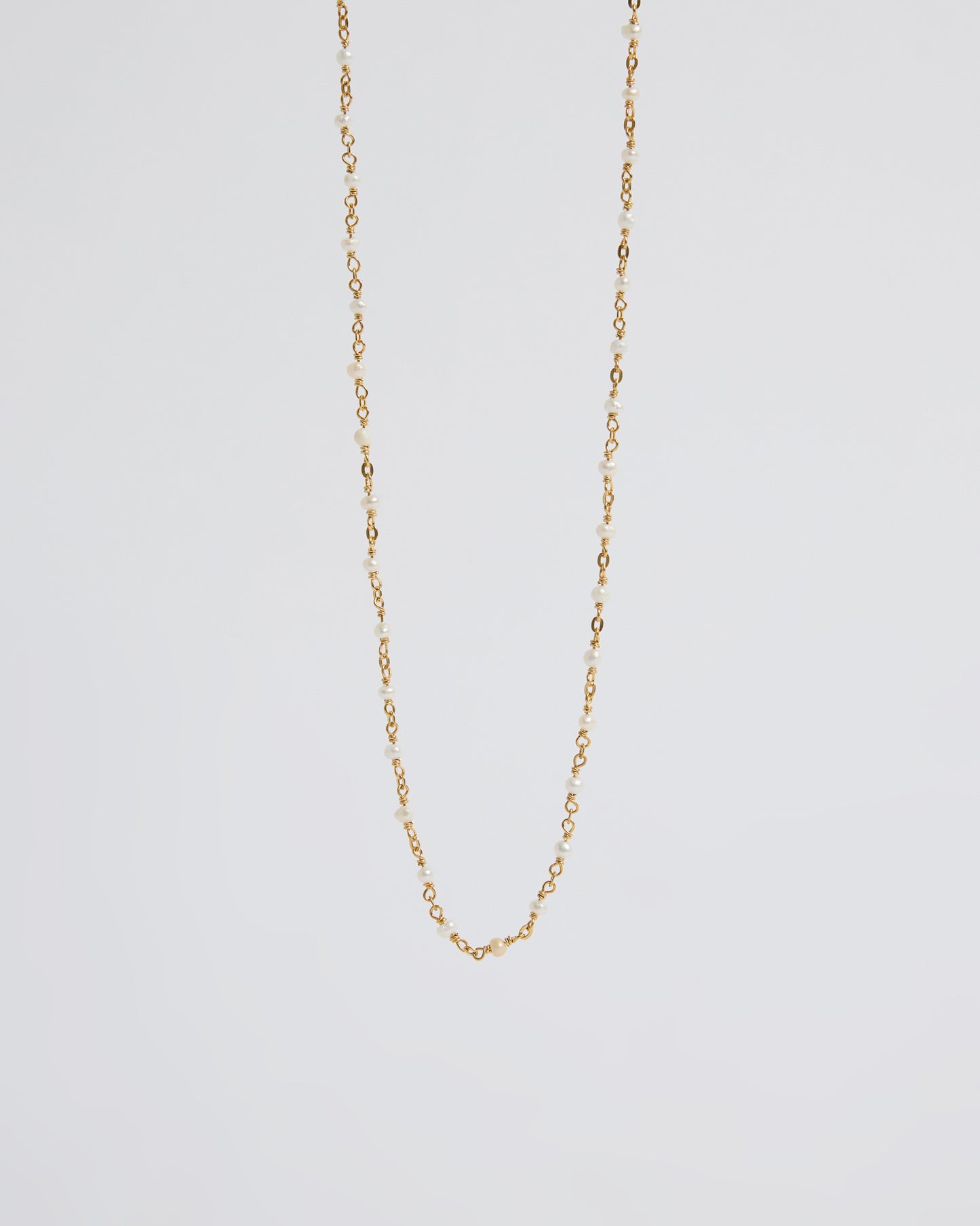 a long delicate pearl necklace draped naturally over the hand