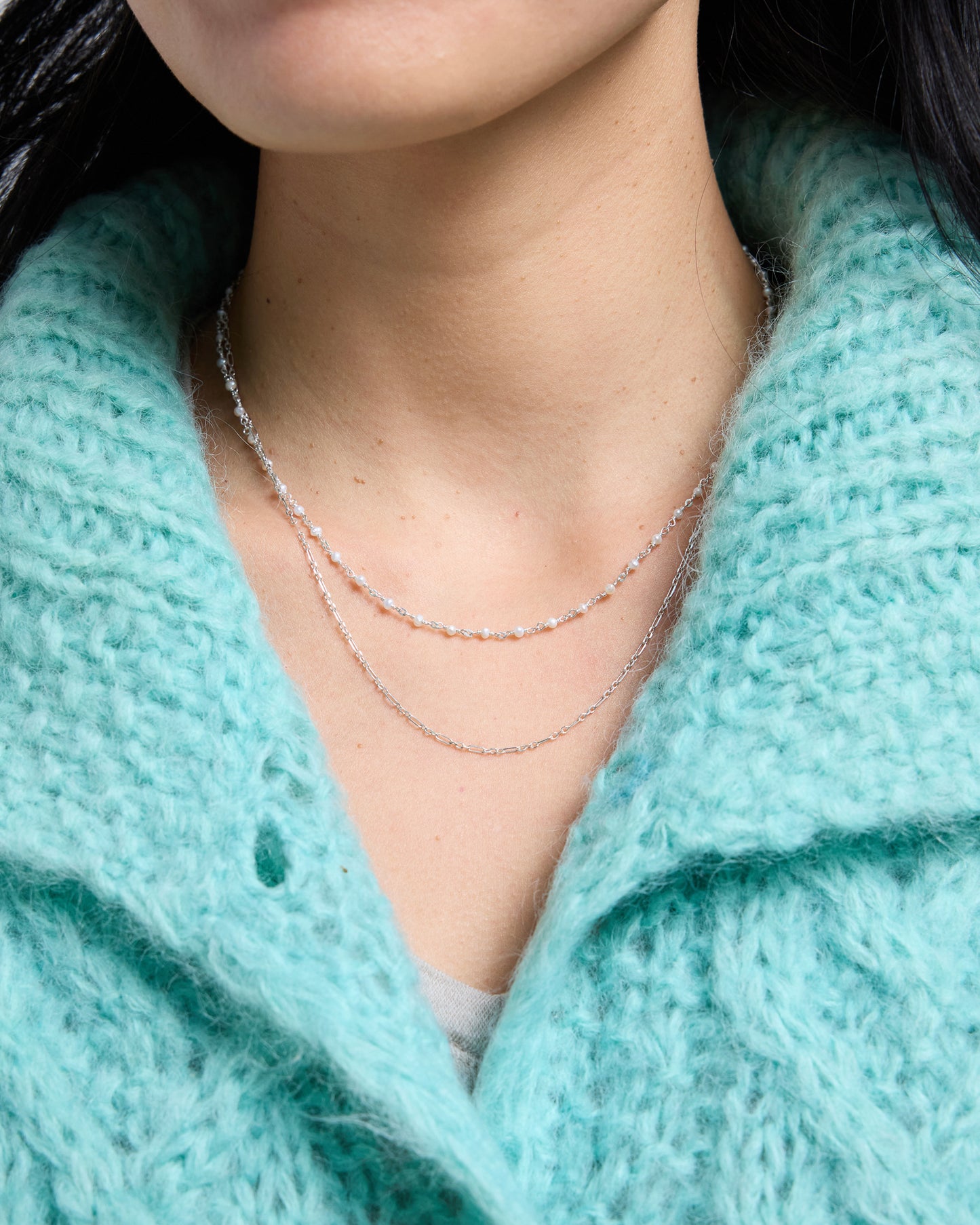 a layered necklace with a pearl chain and a simple silver chain worn together on the neck