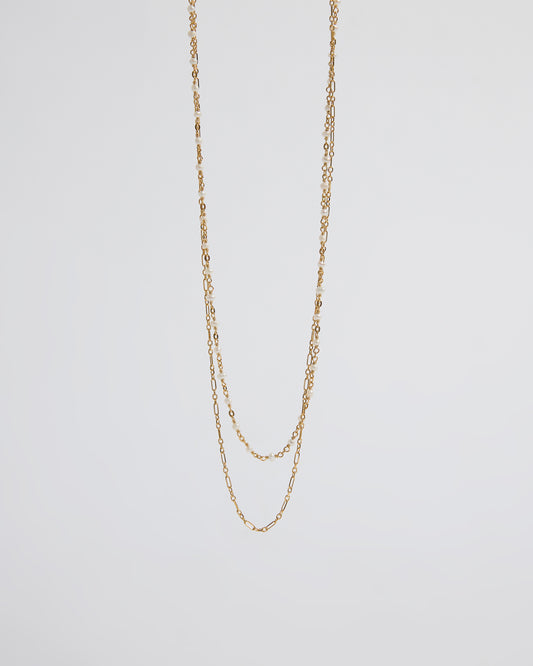 a long layered necklace draped over the hand showing pearl and chain contrast