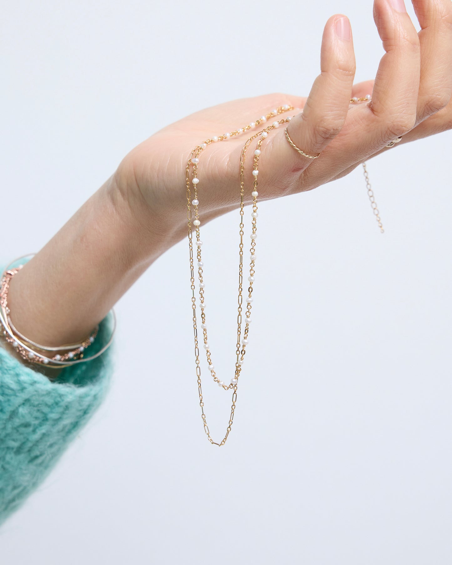 Hand wearing a gold chain necklace on a light gray background