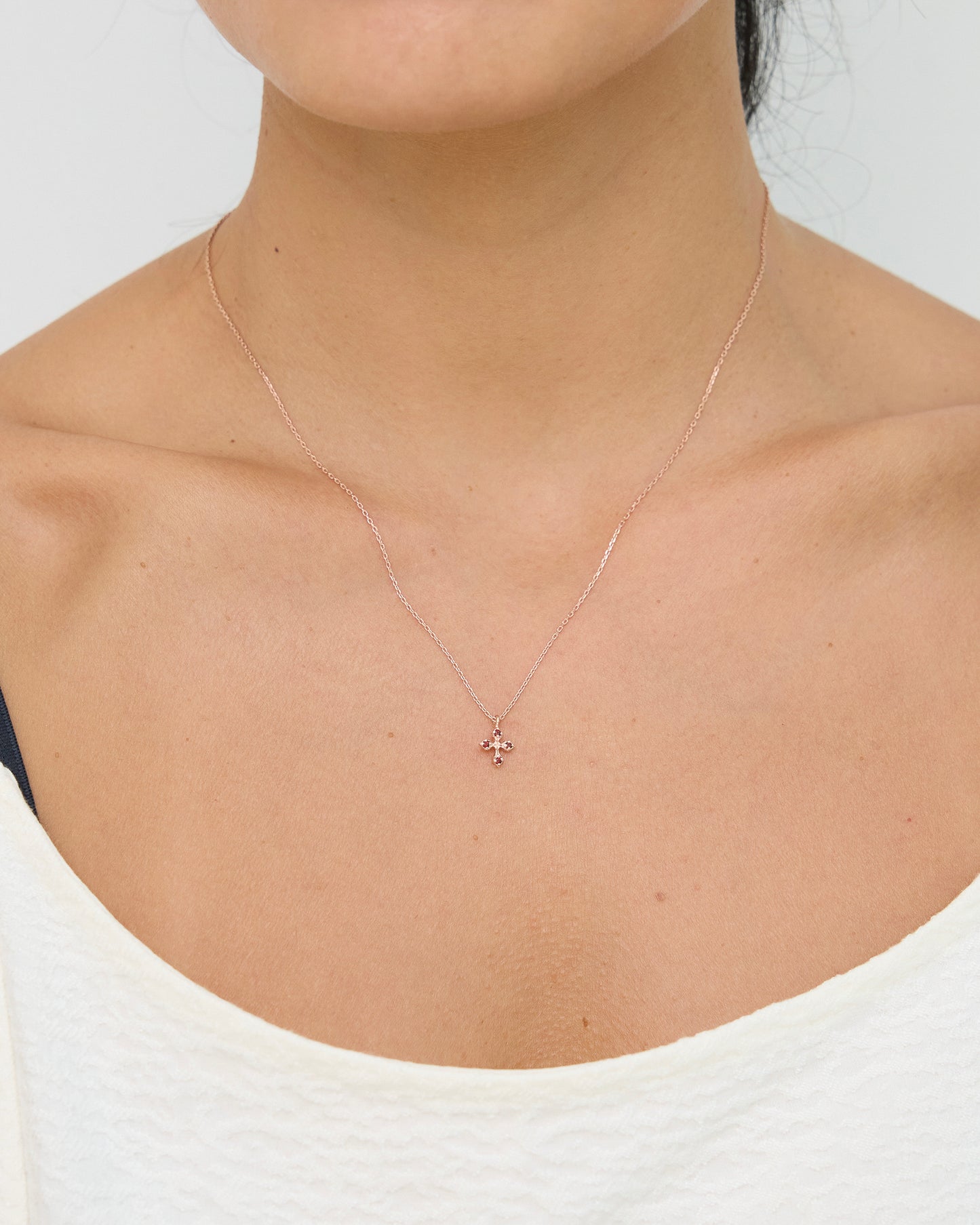 Rose gold necklace with a small pendant on a person wearing a white top.