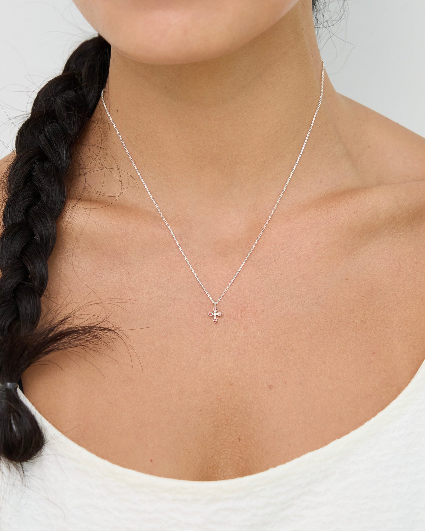 Person wearing a delicate silver necklace with a small pendant on a plain background