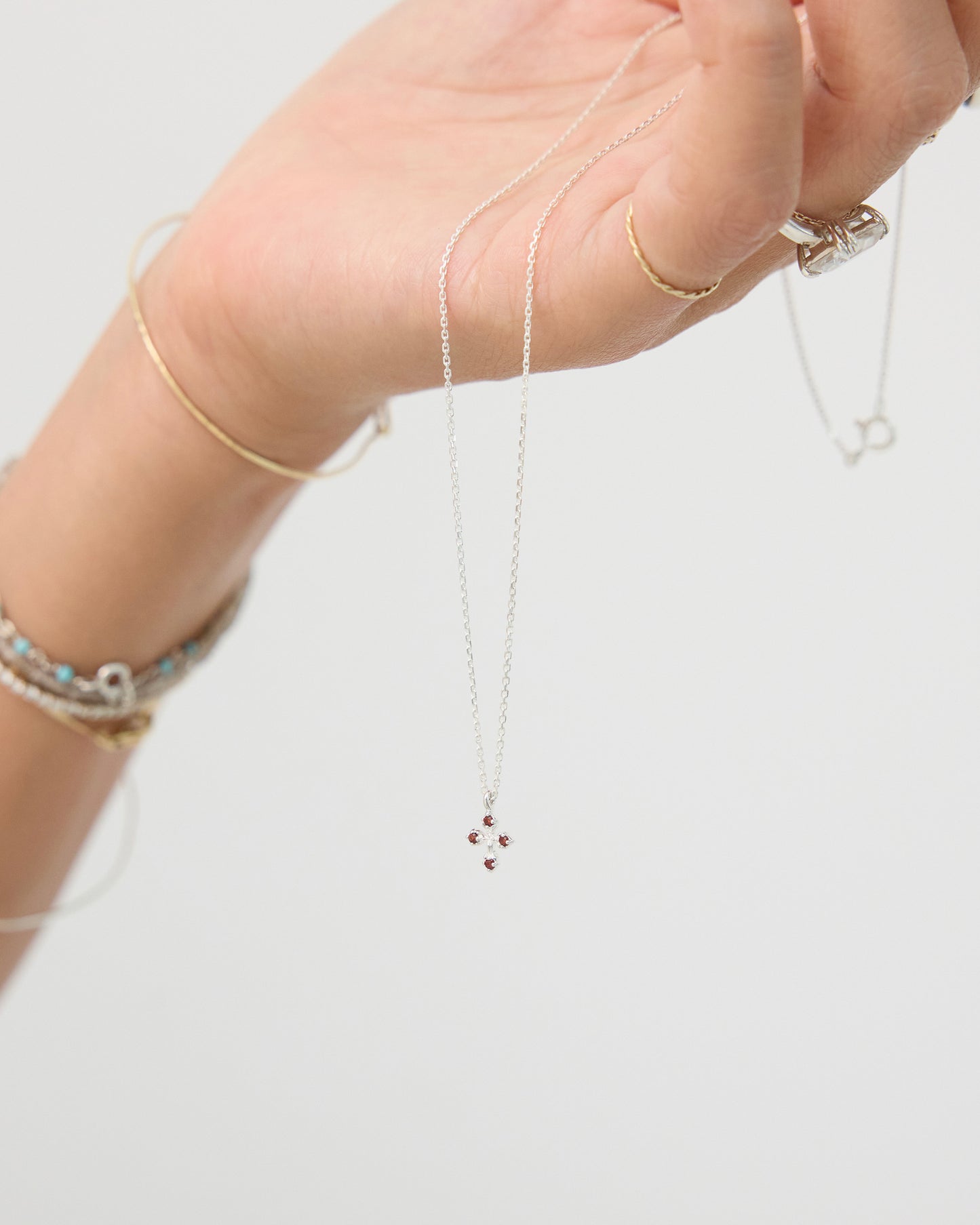 Hand wearing a delicate necklace with small beads on a plain background