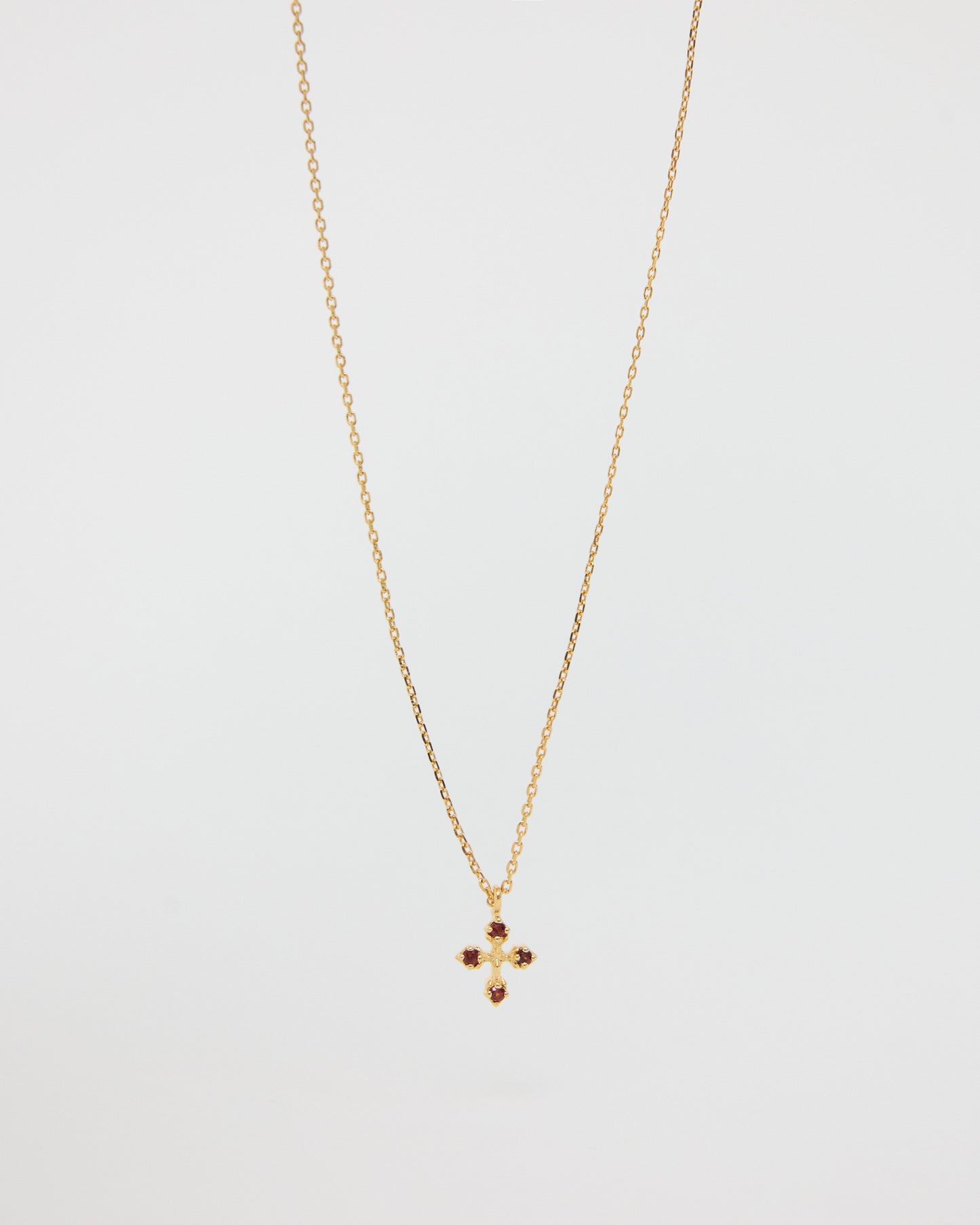 Gold necklace with a small cross pendant on a light gray background