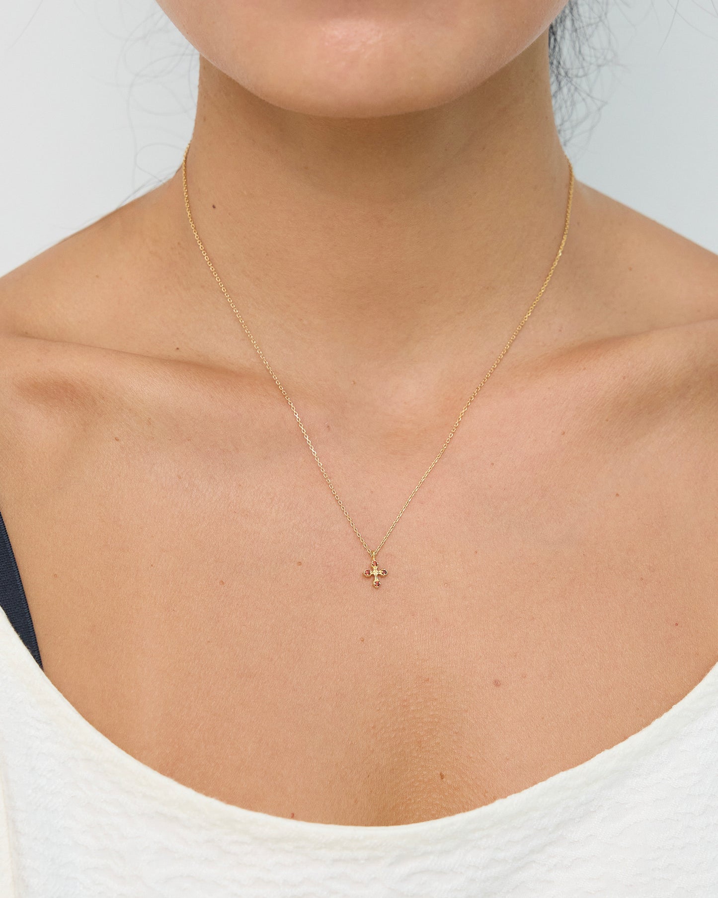 Gold necklace with a small pendant worn by a person against a neutral background