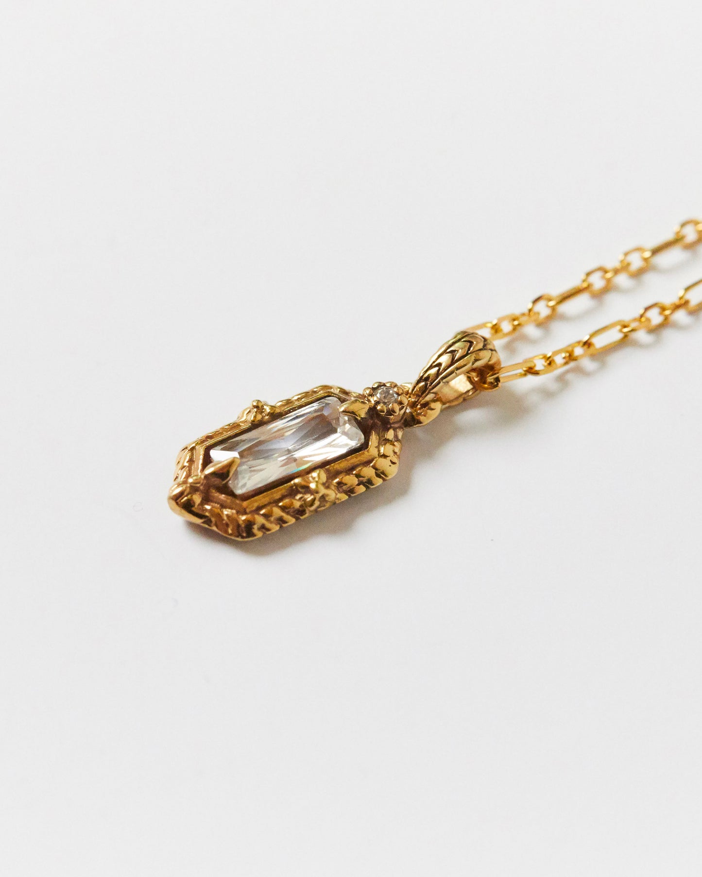 Gold necklace with a clear gemstone pendant on a white background