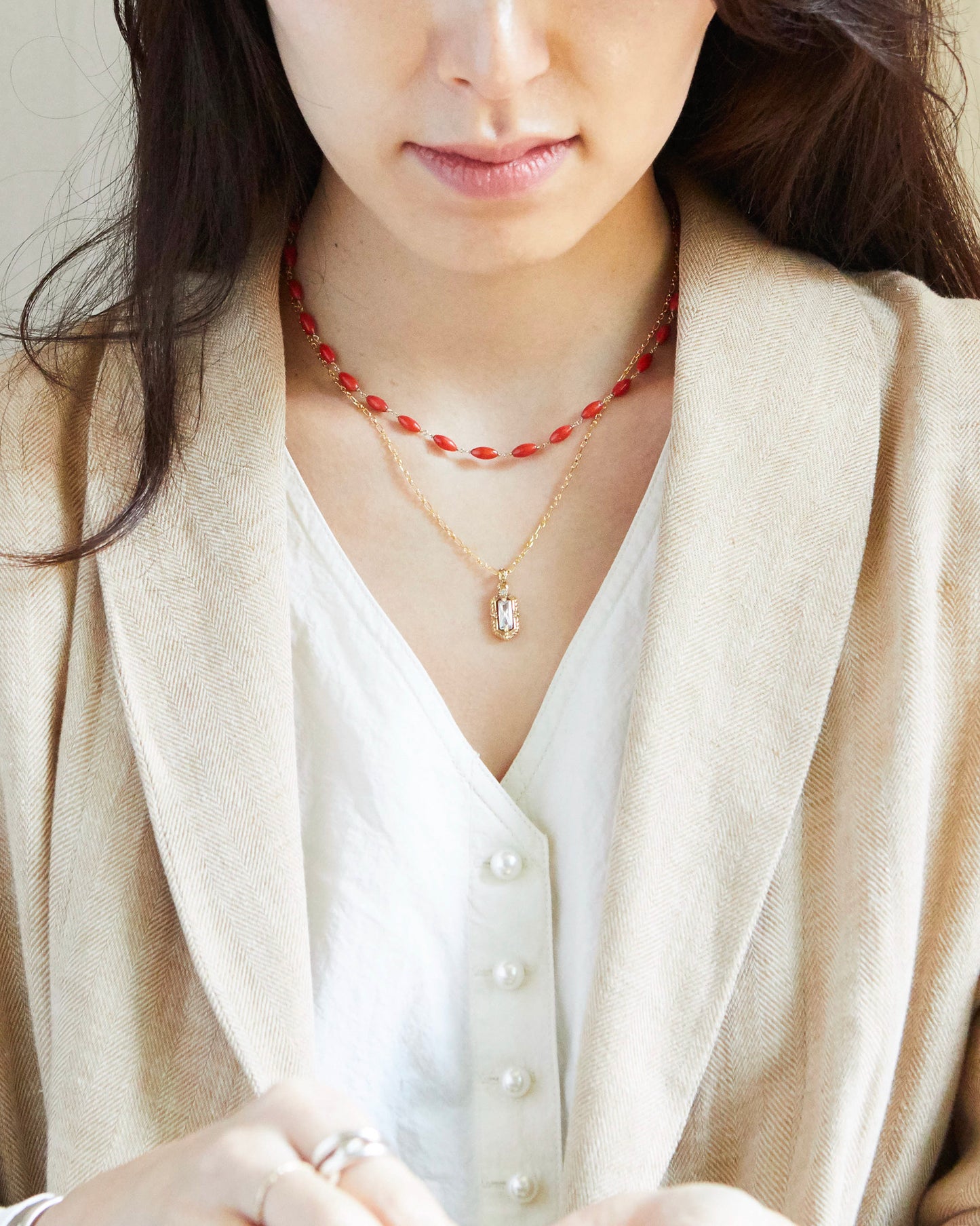 Woman wearing a beige blazer and white shirt with layered necklaces.