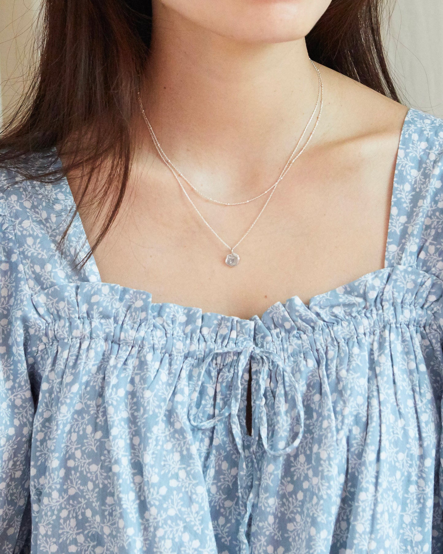 Double-layered 925 silver necklace with textured round pendant on white background