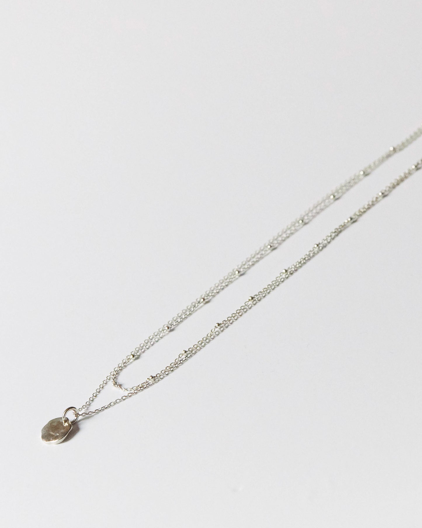 Close-up of hammered silver pendant on fine chain, part of a layered necklace set