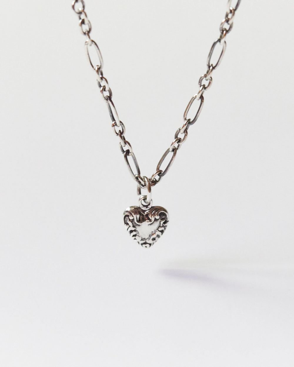 Close-up of a silver heart pendant necklace with mixed chain on skin
