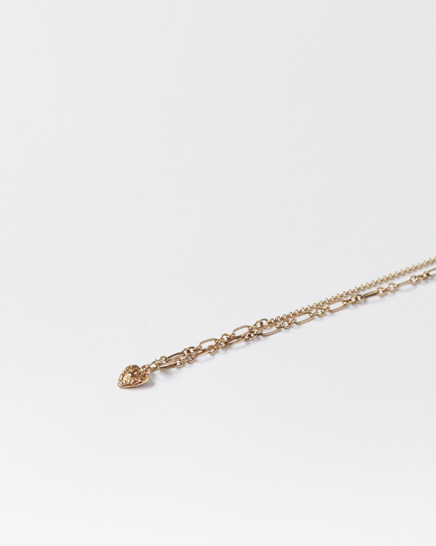 Silver heart pendant hanging from chain mid-air on white backdrop
