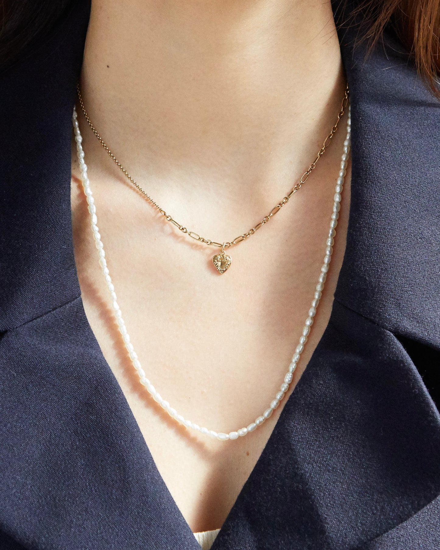 Gold-toned heart pendant necklace styled with gold rings and navy outfit
