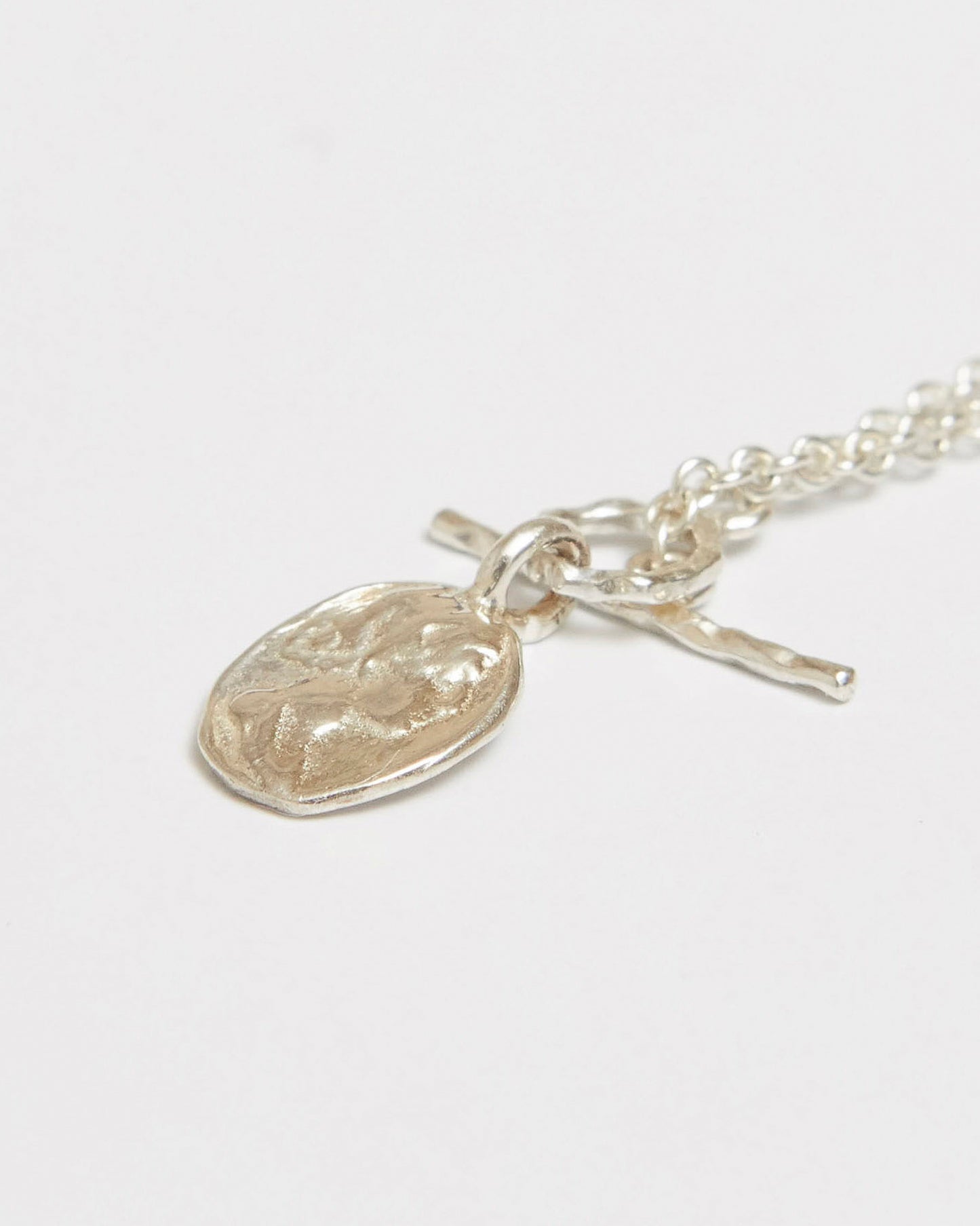 Silver venus necklace with a textured pendant on a light gray background
