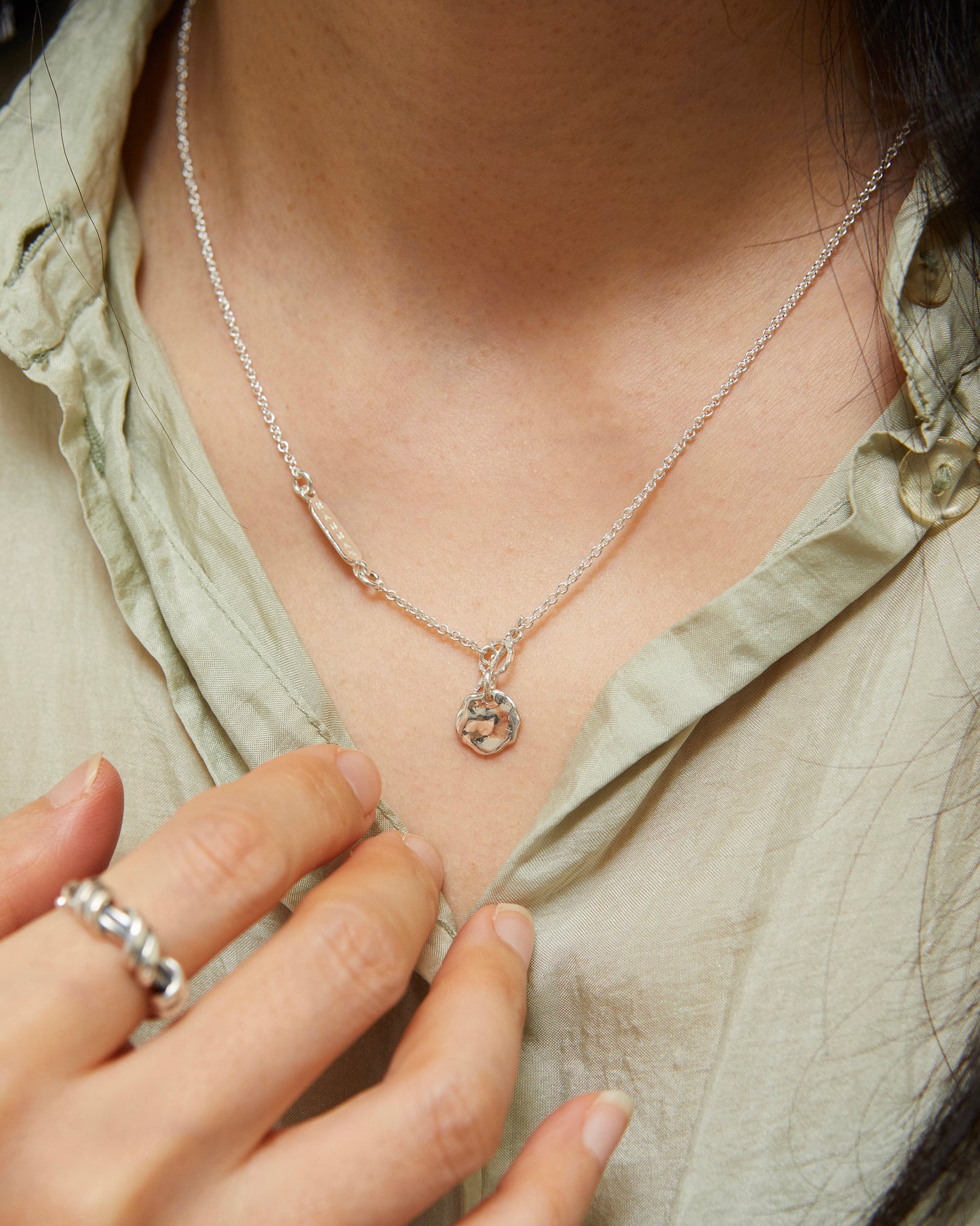 Close-up of silver pendant necklace styled with casual outfit