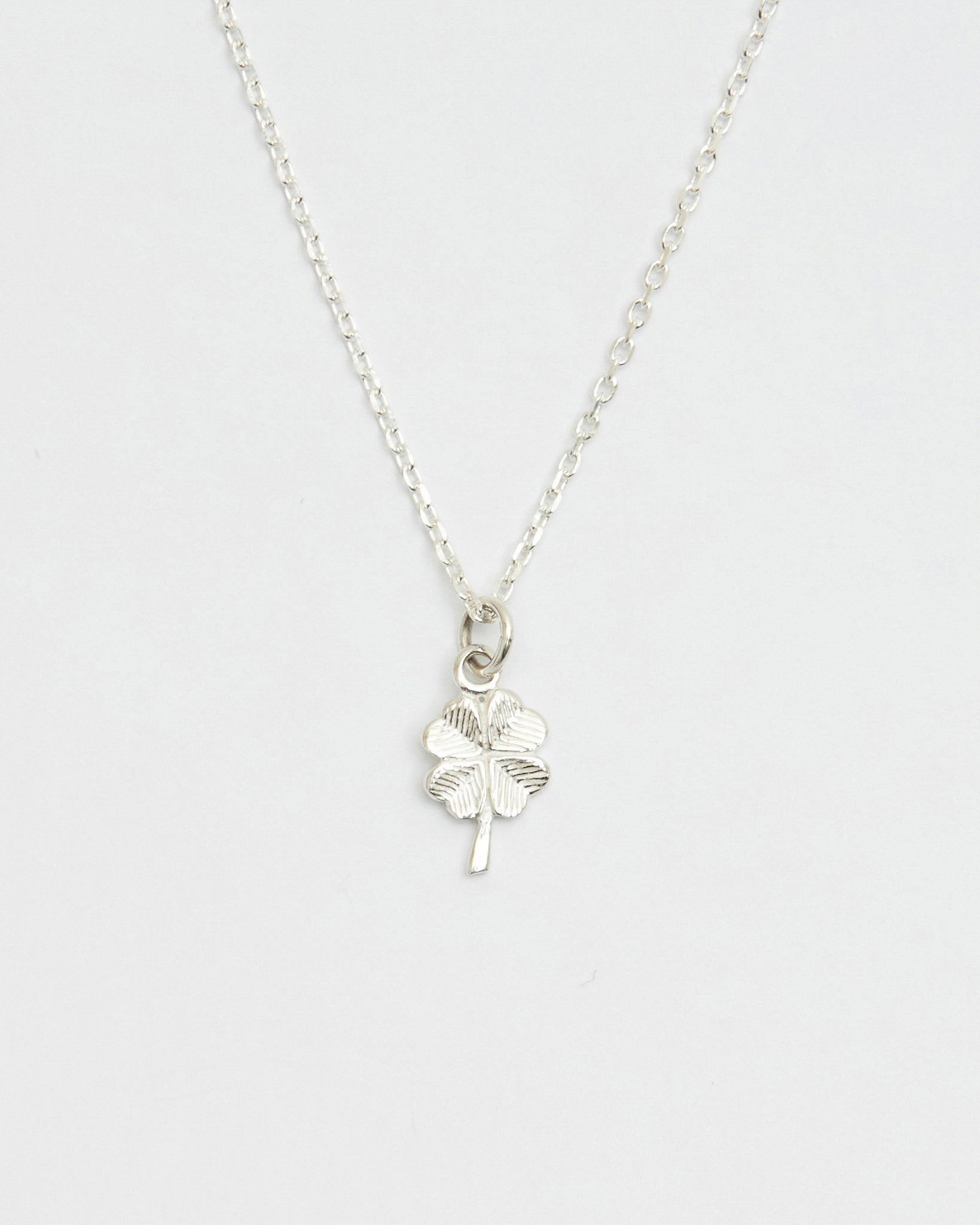 Minimal silver four leaf clover necklace displayed on white background