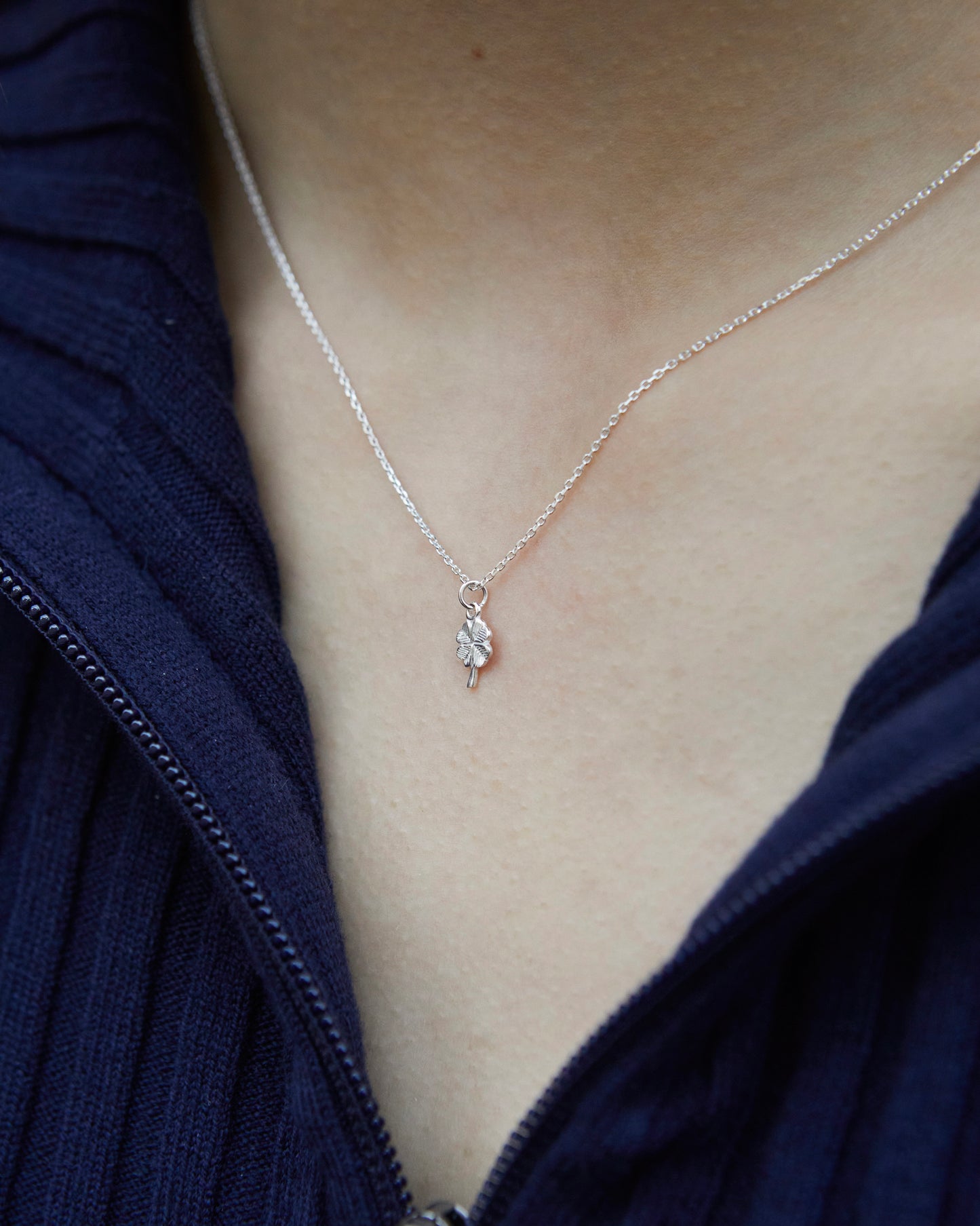 Minimal silver four leaf clover necklace worn on neck, delicate lucky charm necklace for everyday styling
