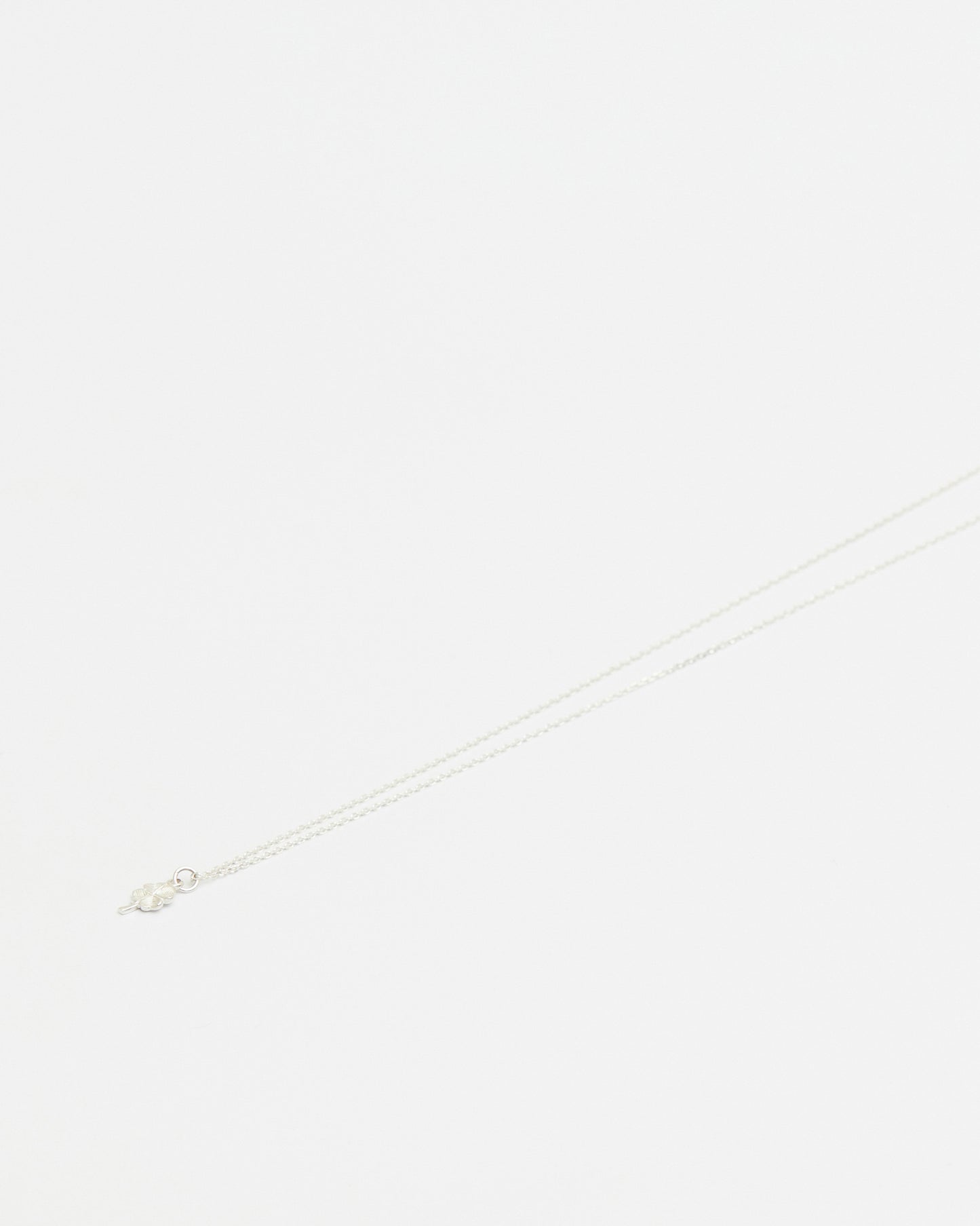 Close-up of delicate silver four leaf clover pendant necklace on white background