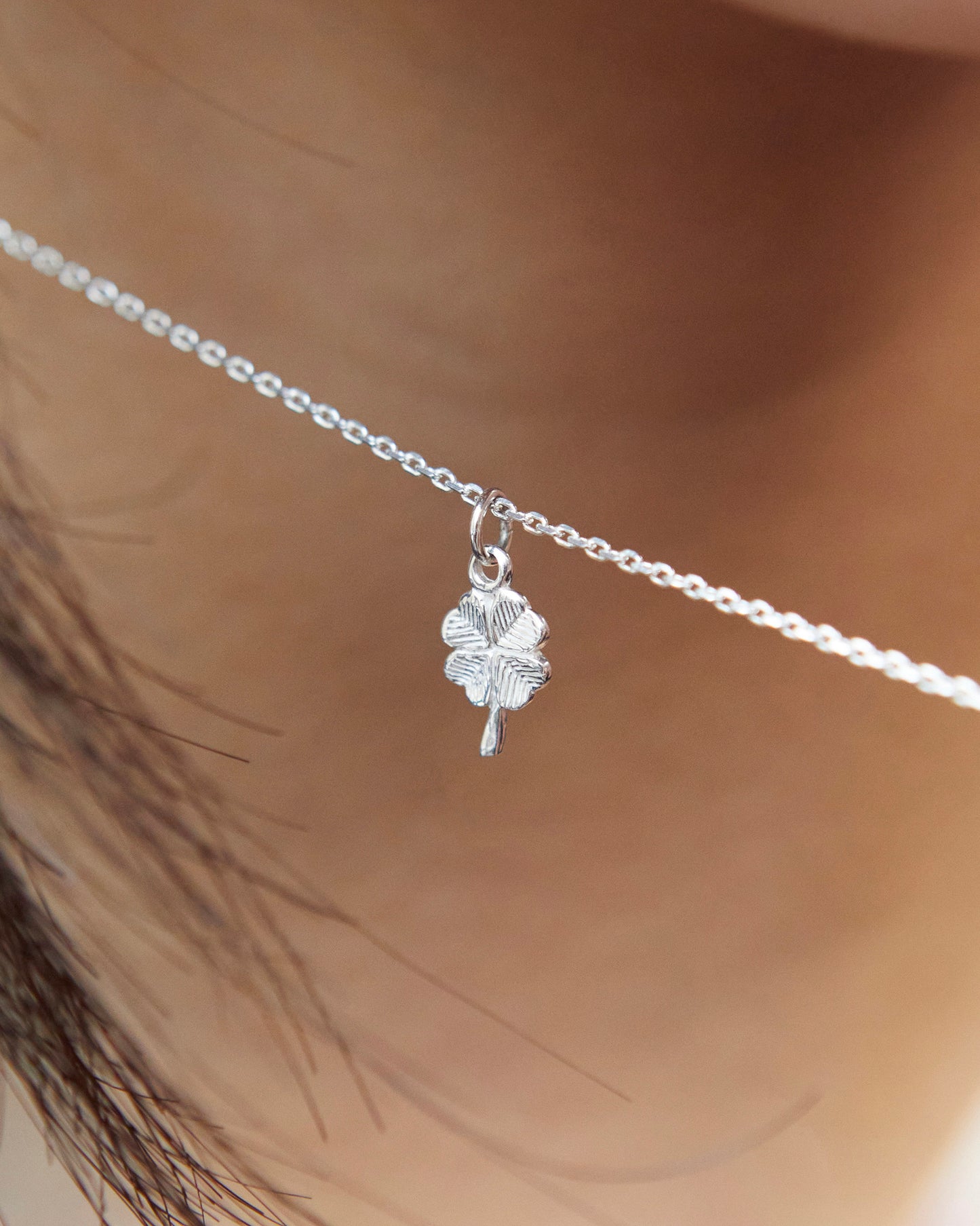 Detailed close-up of silver four leaf clover charm necklace with textured pendant
