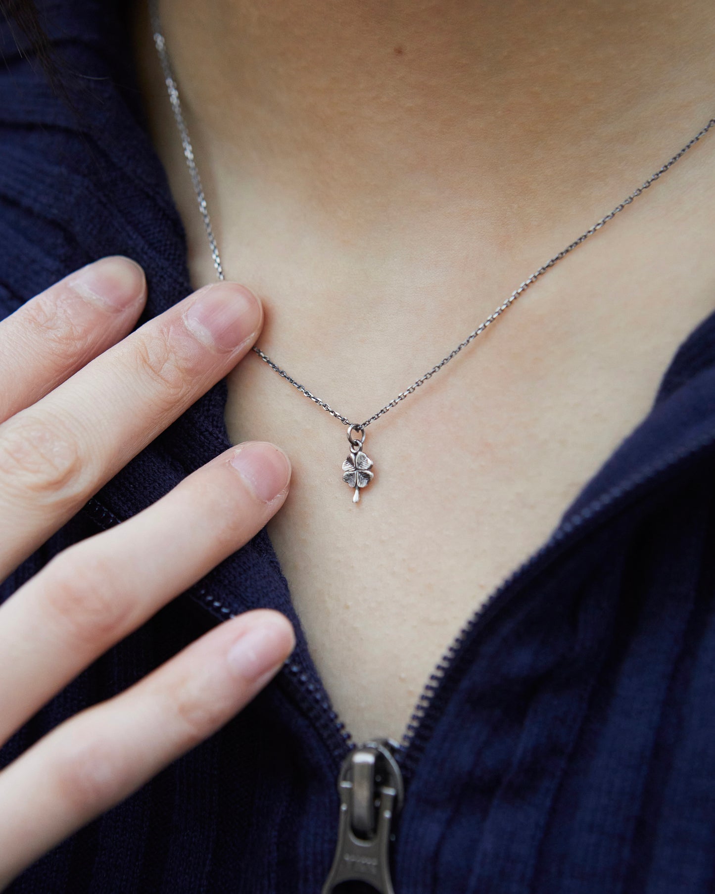 Delicate antique silver clover necklace worn with hand detail, minimalist lucky jewelry styling