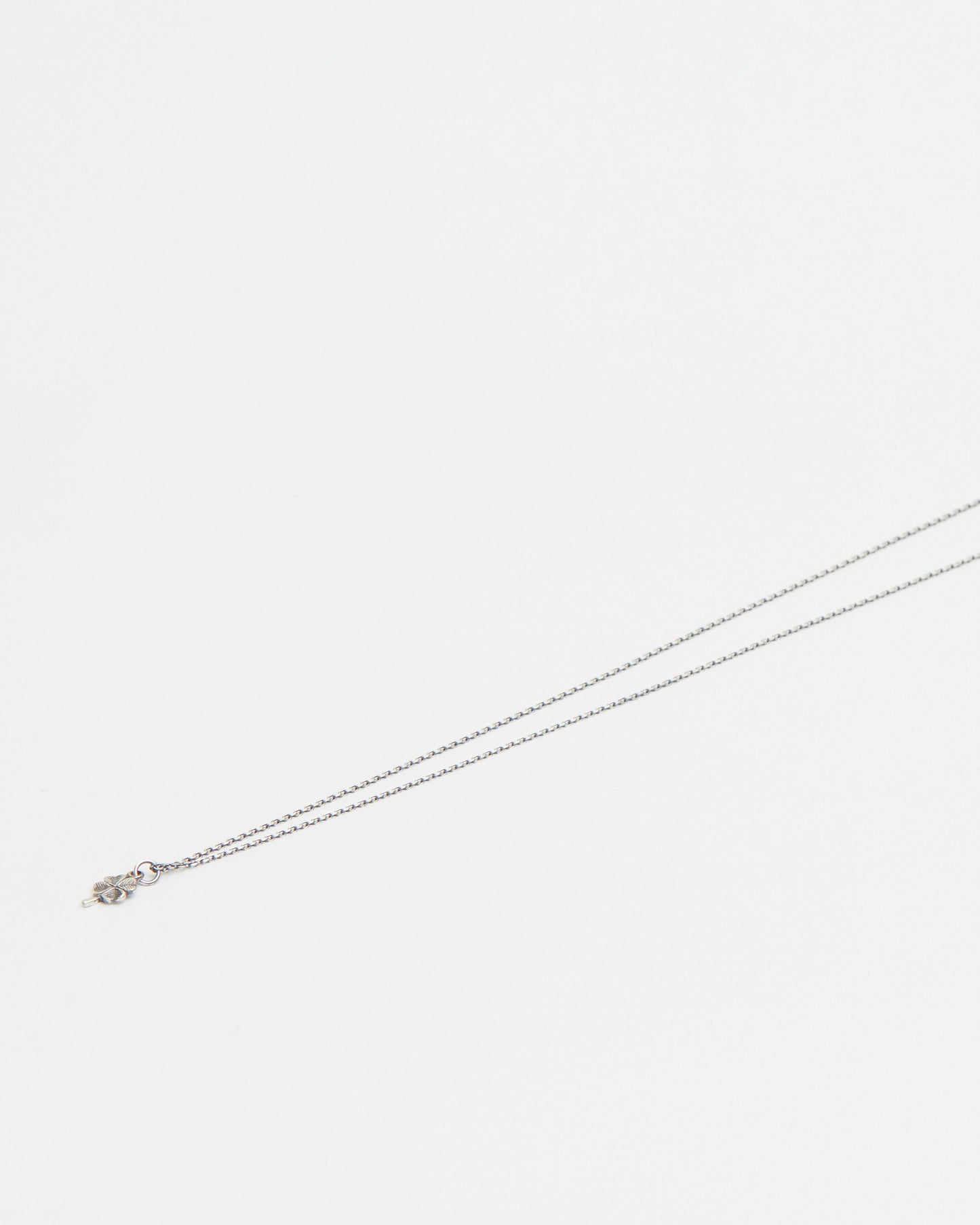 Close-up of delicate antique silver four leaf clover pendant necklace on white background