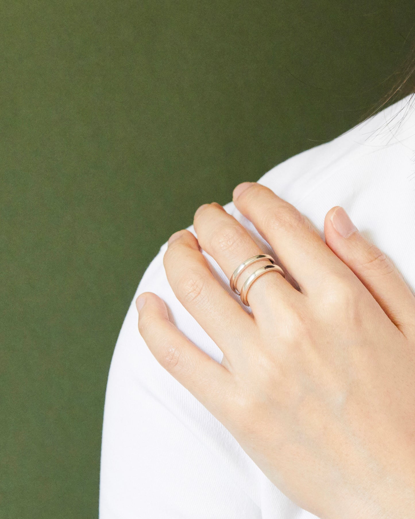 Minimal sterling silver double-line ring styled on hand against soft fabric, featuring sculptural open silhouette and clean contemporary jewelry aesthetic.