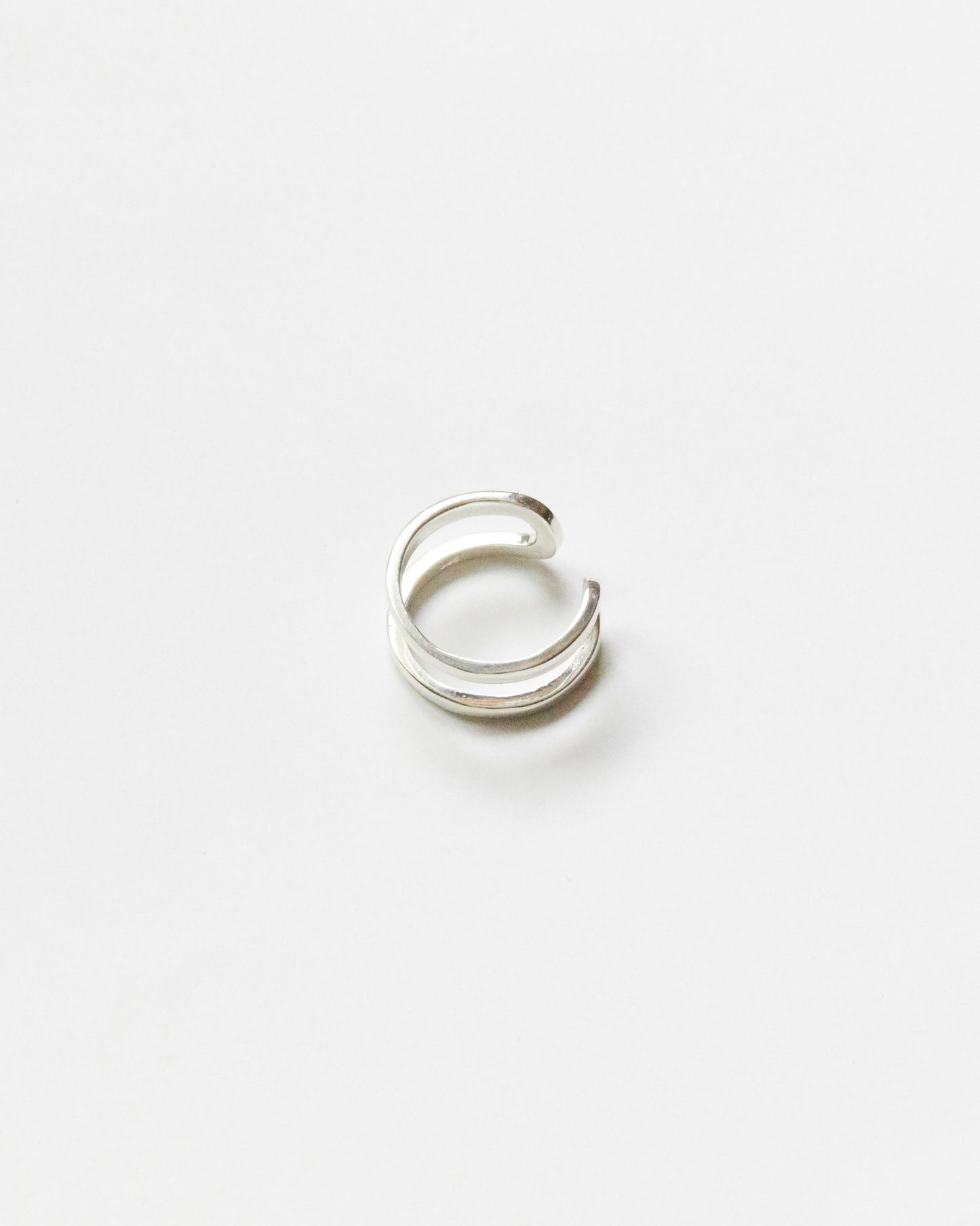Minimalist sterling silver double-line ring with open sculptural shape displayed on clean white background for modern jewelry product photography.