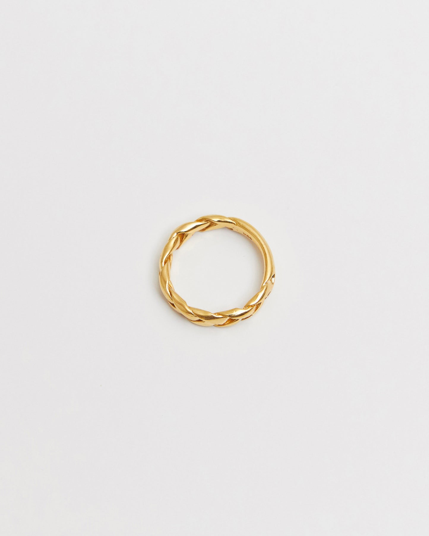 Close-up of a gold braided ring resting on a white background, showcasing its twisted woven design.