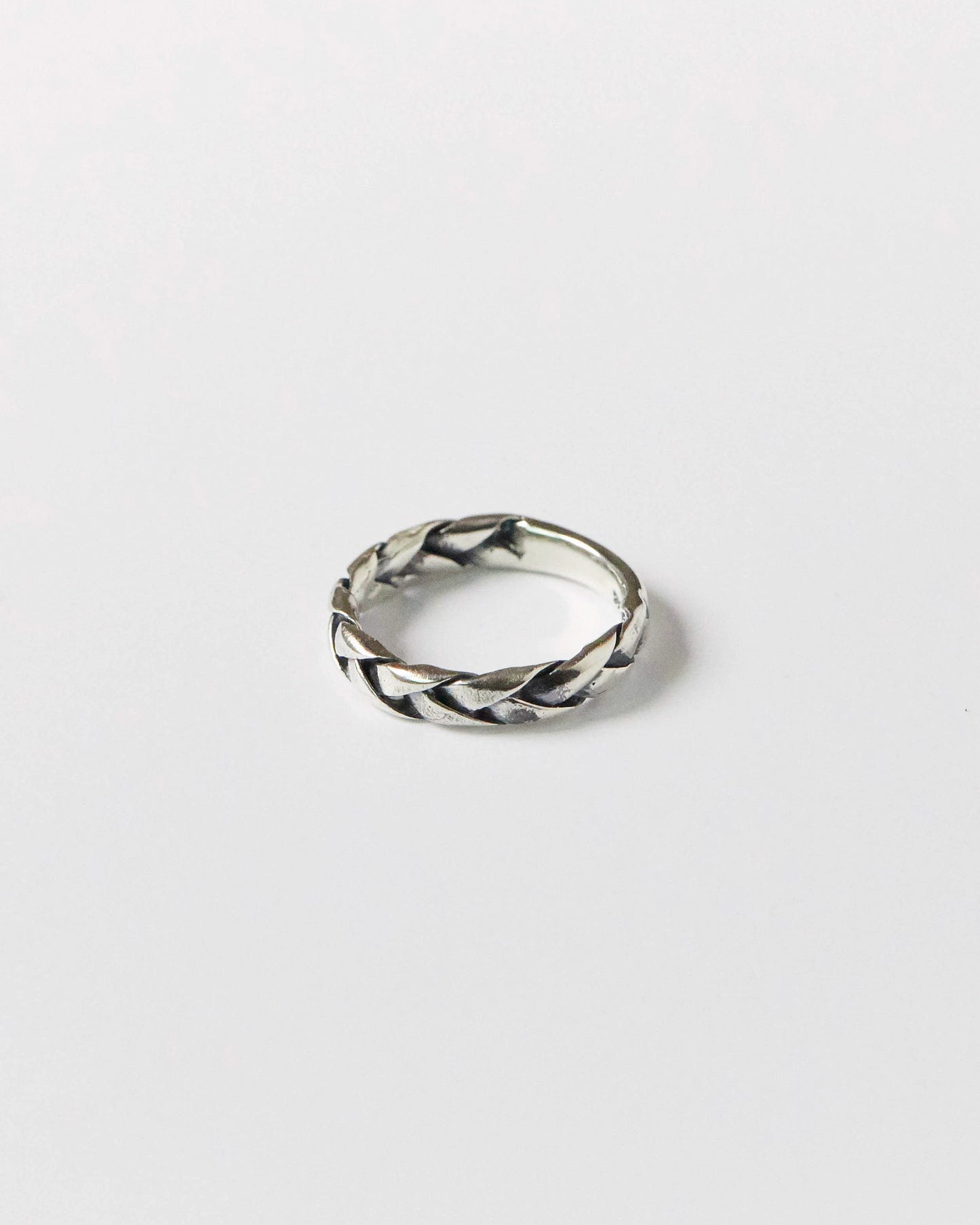 Close-up of a antique silver braided ring resting on a white background, showcasing its twisted woven design