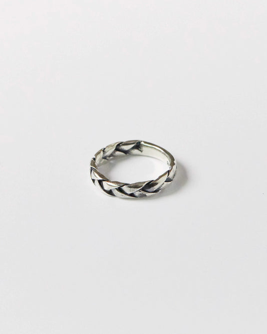 Close-up of a antique silver braided ring resting on a white background, showcasing its twisted woven design